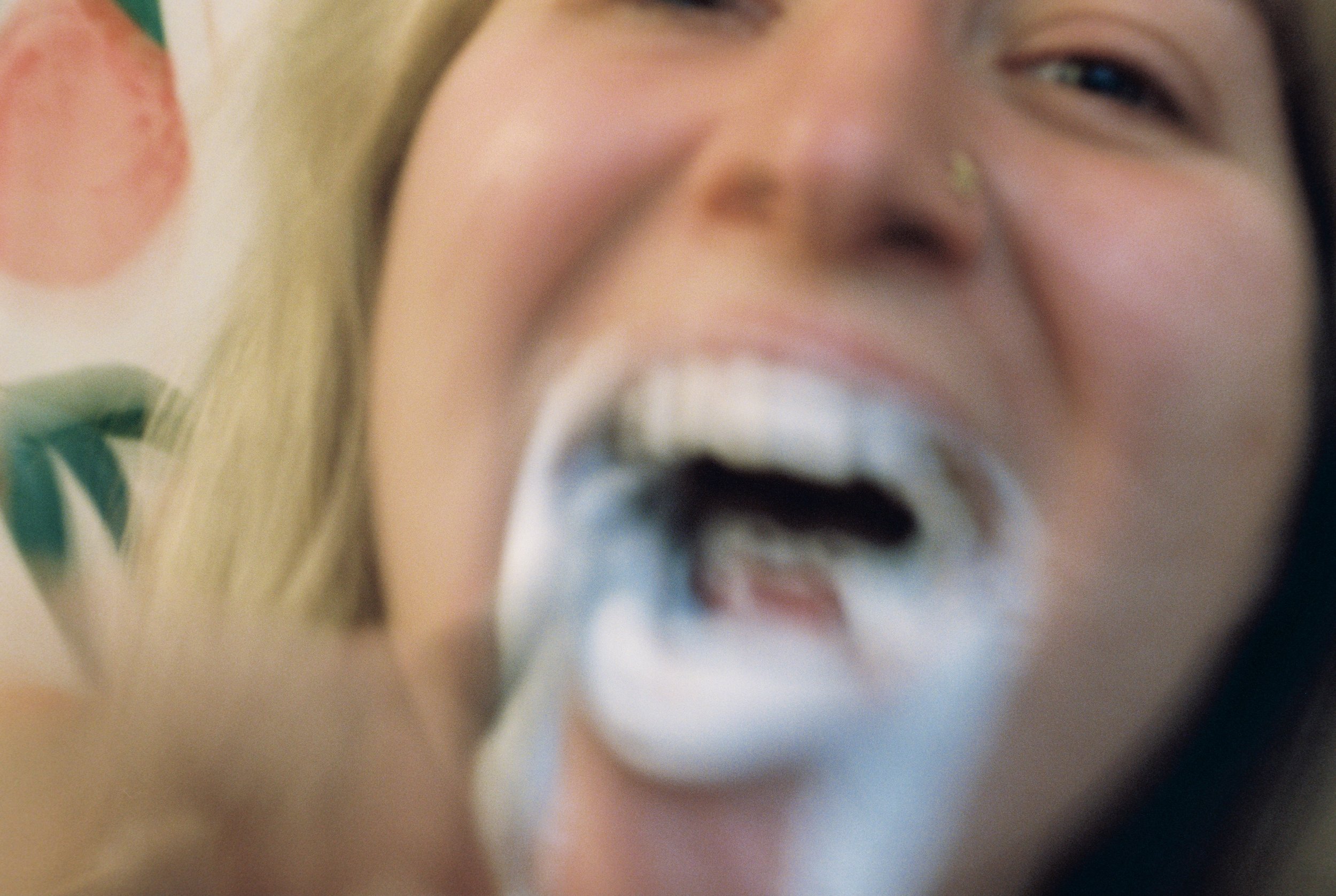 Close-up of a person with foam around their mouth, smiling and looking into the camera, with part of a colorful pattern or fabric in the background.