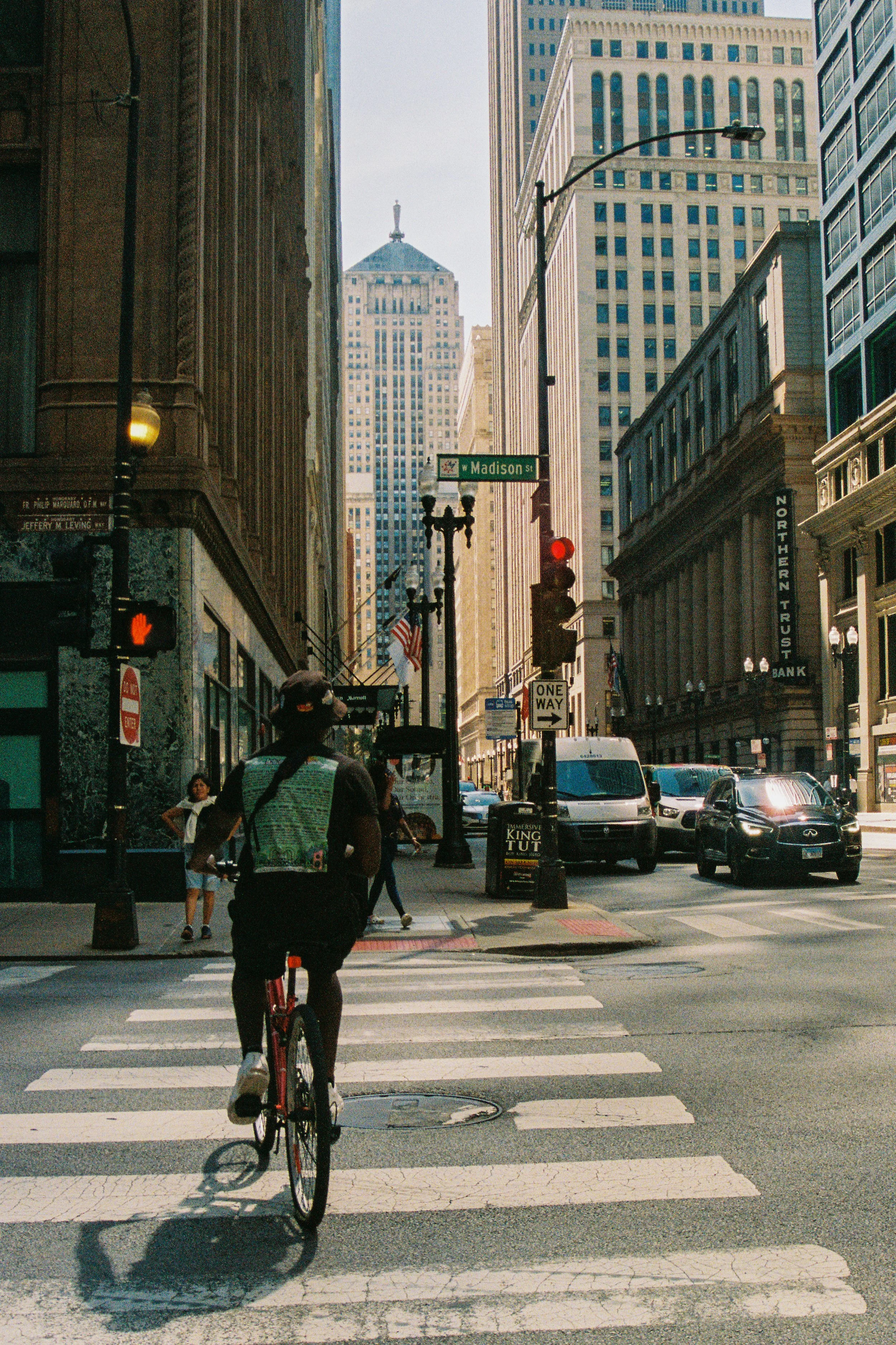 A person riding a bicycle across a crosswalk in an urban city with tall buildings, street signs, and vehicles.