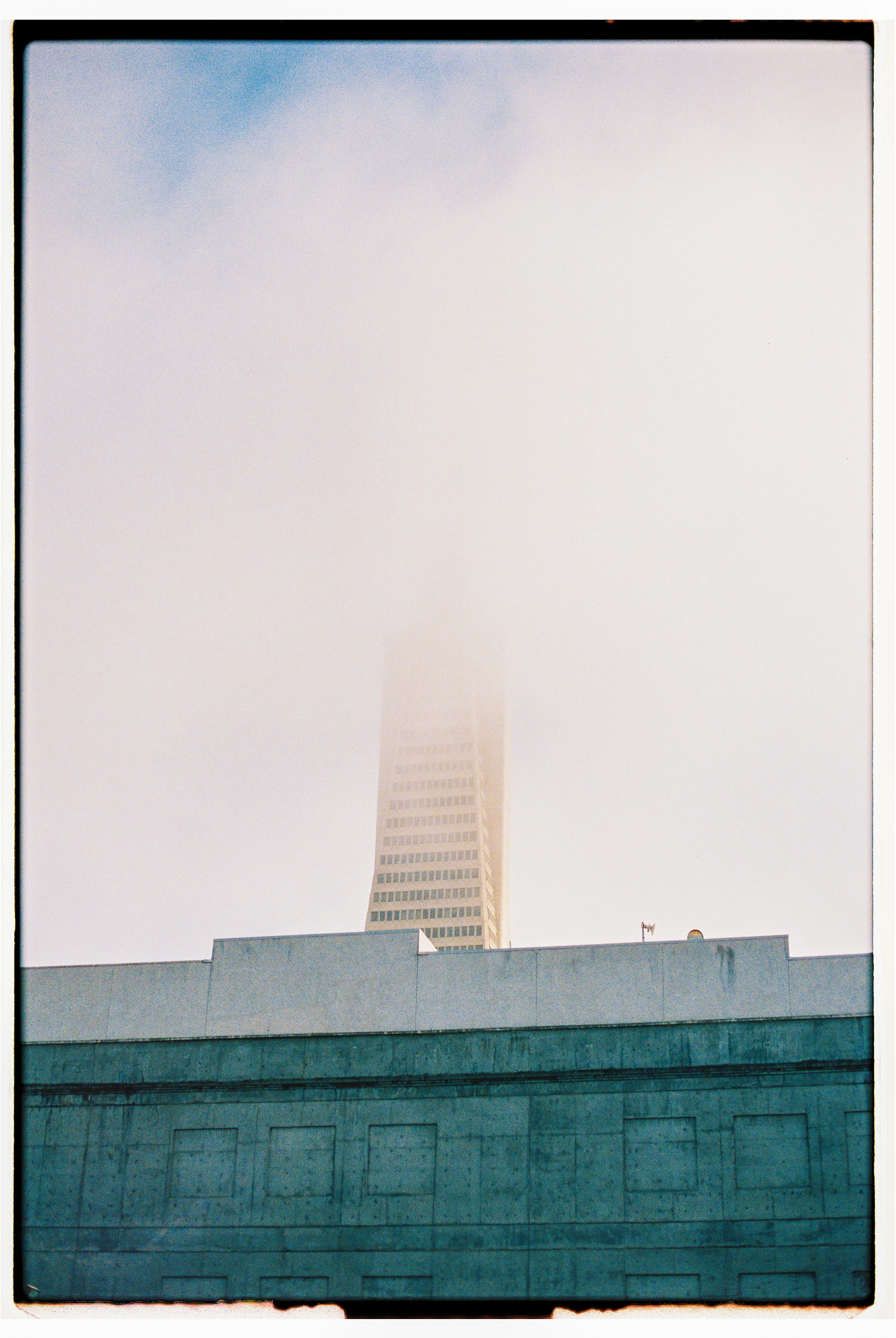 A tall building partially covered by fog, with a lower building in the foreground.