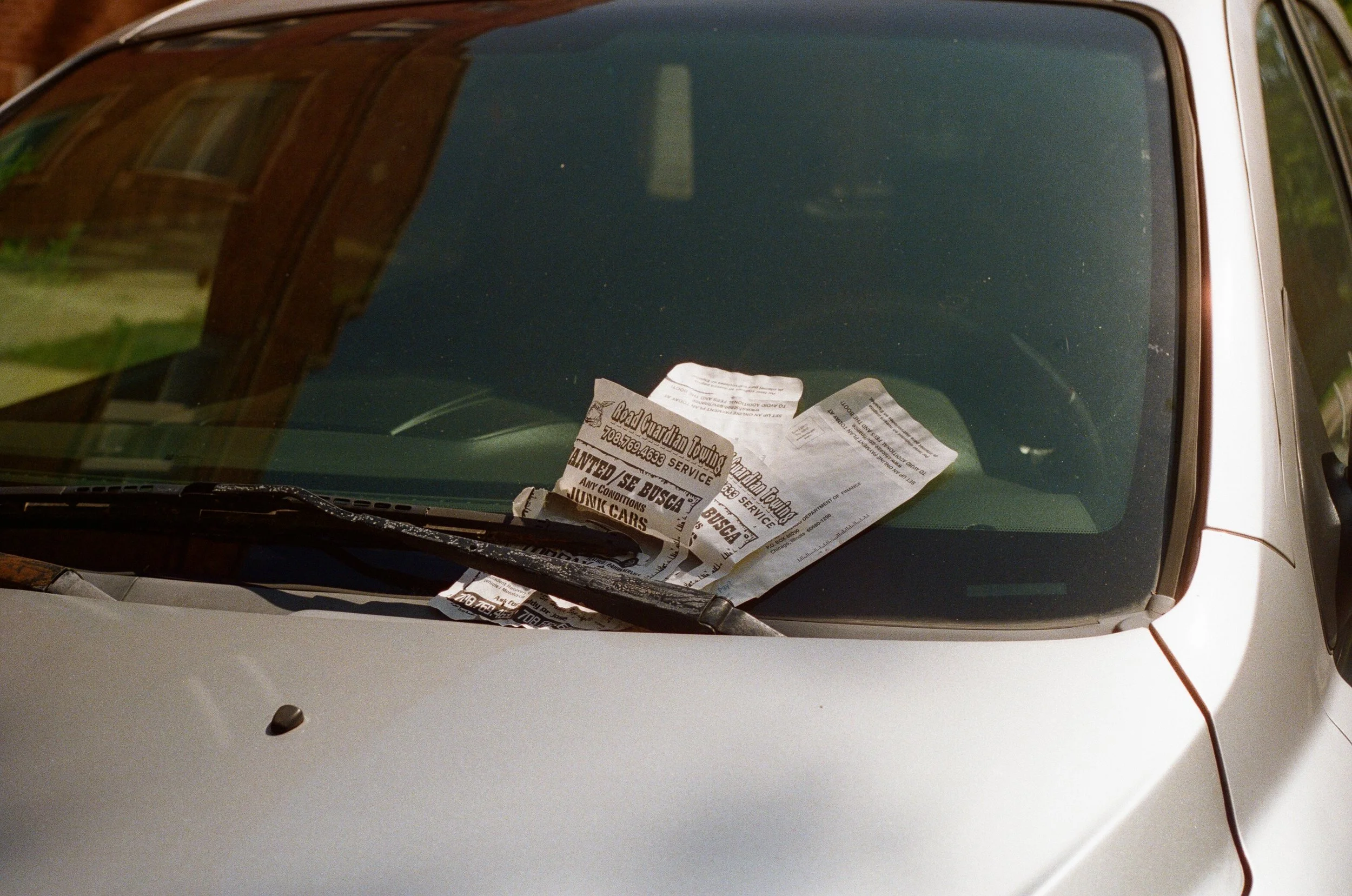 A car with a wrinkled paper sign placed on the dashboard under the windshield wiper.