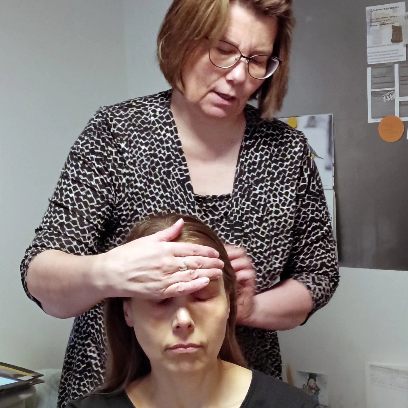 Rauha tekee lempeämpää ja syvärentouttavaa intialaista päähierontaa. Kuvassa asiakas nojaa hoitajan toiseen käteen samalla kun hoitaja hieroo toisella kädellä päänahkaa. Päähierontahoito Kuopiossa.