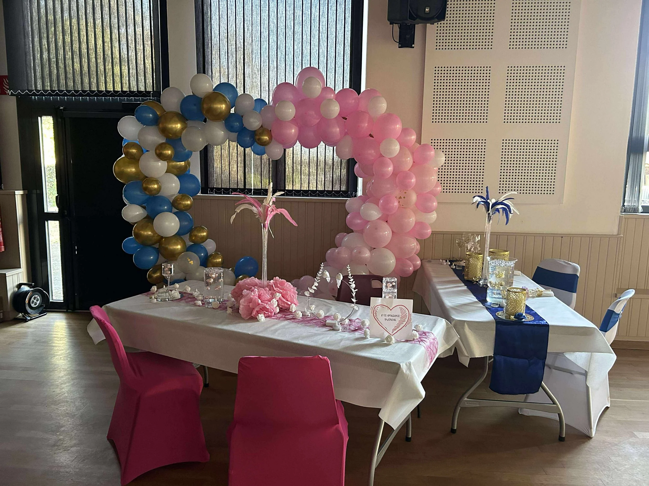 Décoration de fête avec un ballon en forme de cœur pour une célébration dans une salle intérieure, comprenant des ballons colorés, une table avec des objets décoratifs et un centre de table floral.