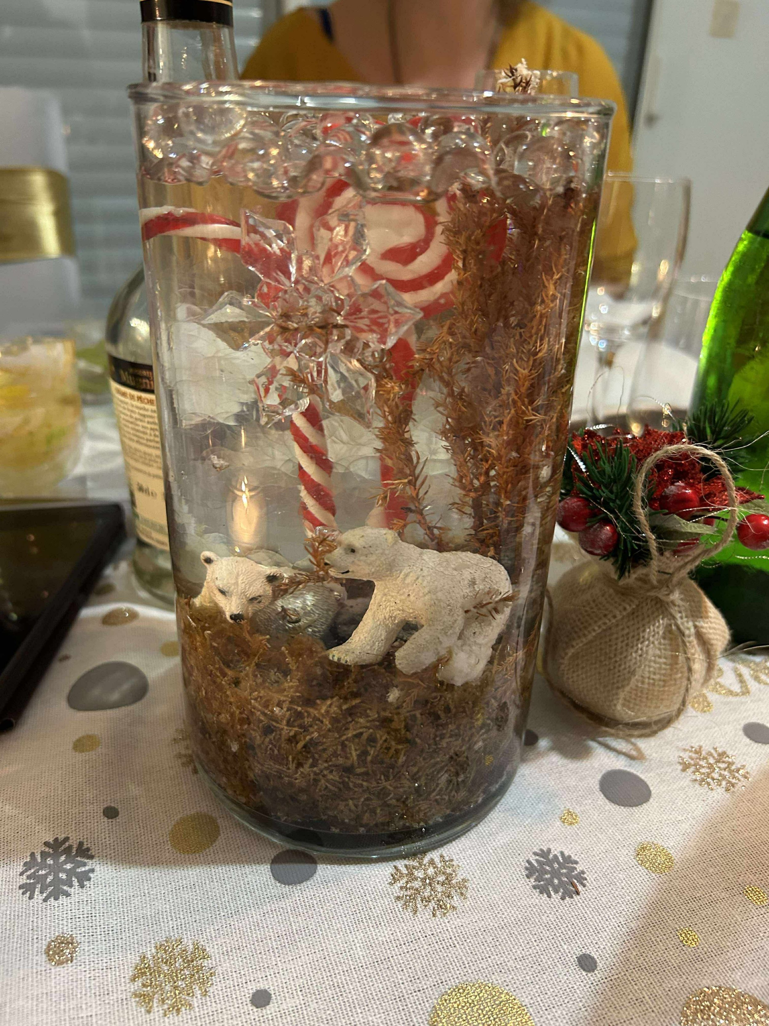 Vase en verre avec décorations de Noël, comprenant des ours polaires en plastique, des branches d'arbres séchées, une étoile en cristal, une canne en sucre de Noël, et des décorations de Noël à l'extérieur.