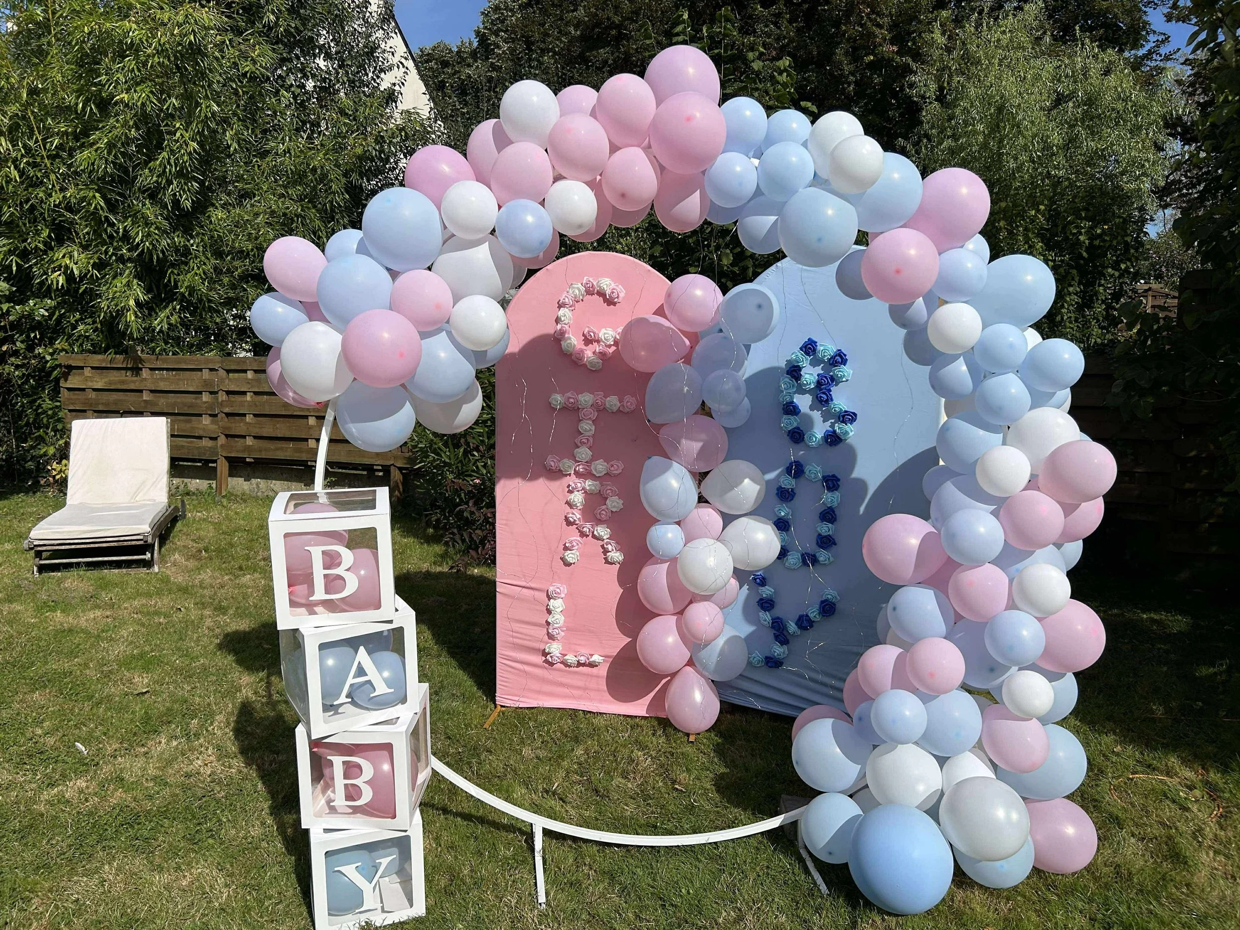 Décoration de fête avec ballon rose, bleu et blanc, arches de ballons, lettres en fleurs formant le mot 'BABY' et numéro '6' pour une célébration d'anniversaire dans un jardin