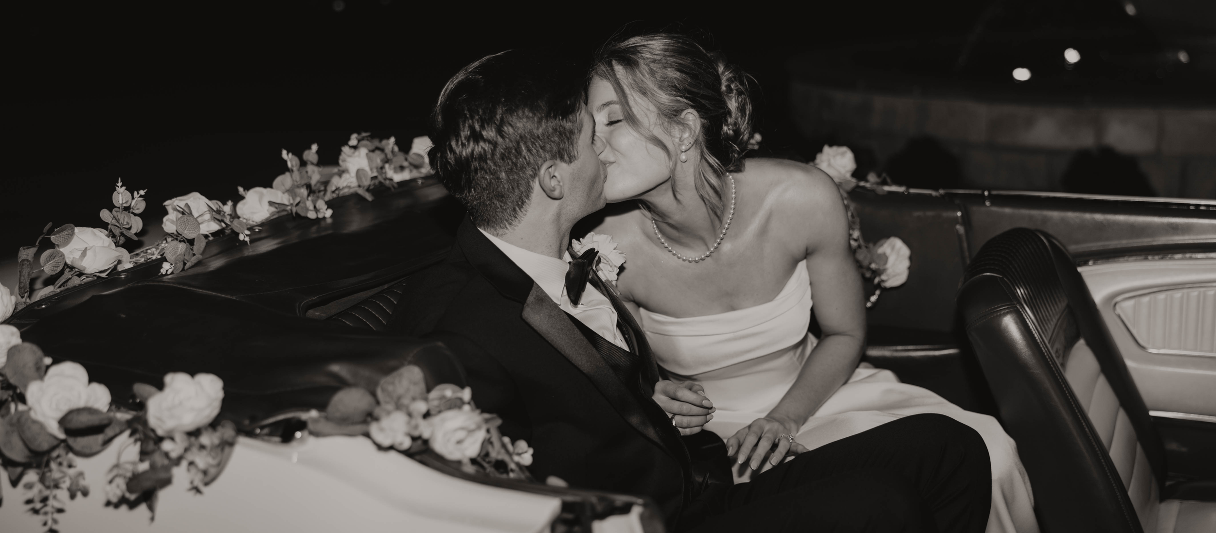 Mariage organisé par A&L events, Photo noir et blanc dun couple de jeune mariés qui s'embrasse dans une voiture décapotable, décorée de guirlande de rose et eucalyptus.