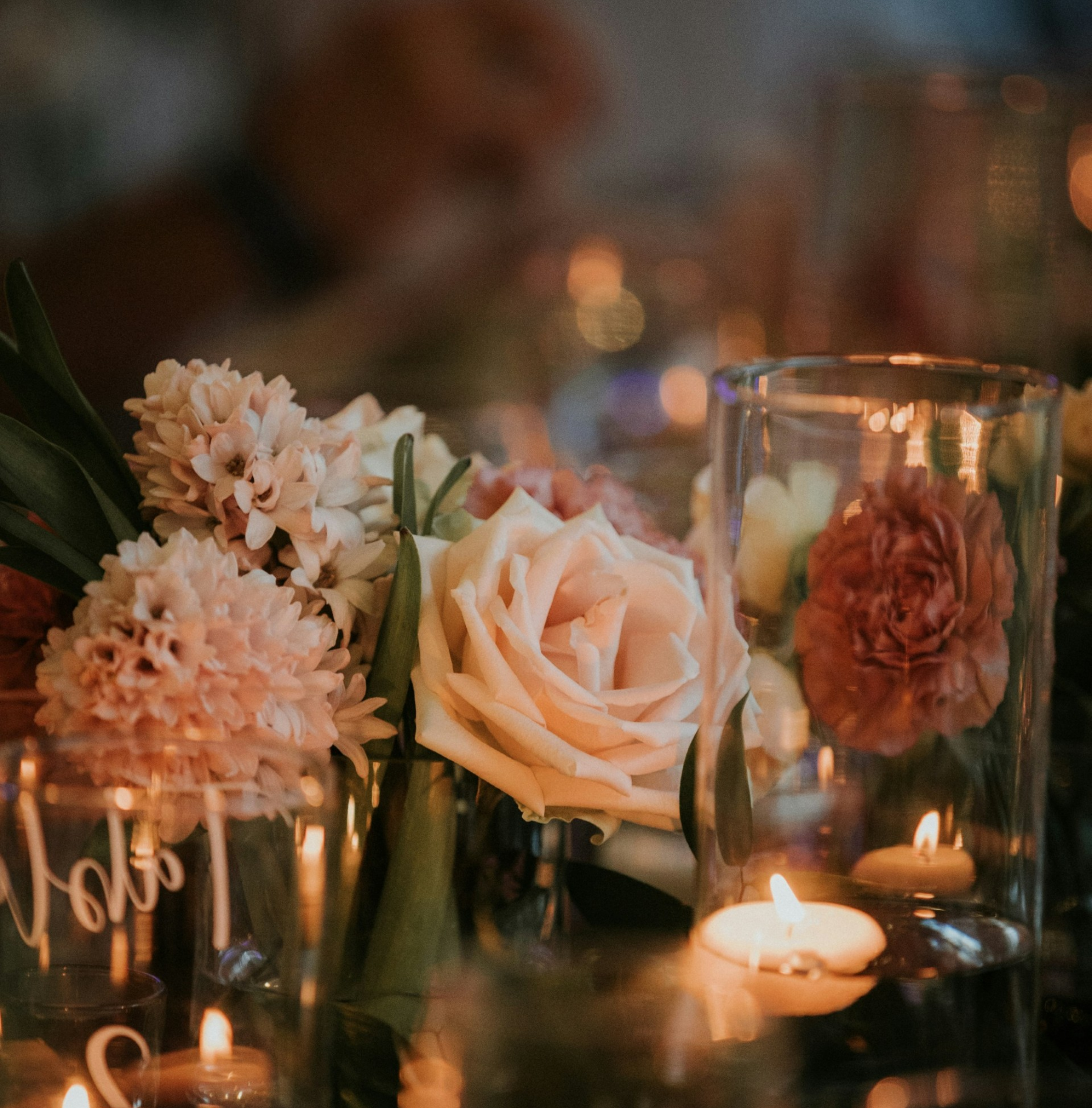 Un arrangement floral avec des roses et des fleurs blanches, décoré avec des bougies dans un vase en verre, ambiance chaleureuse et intime.