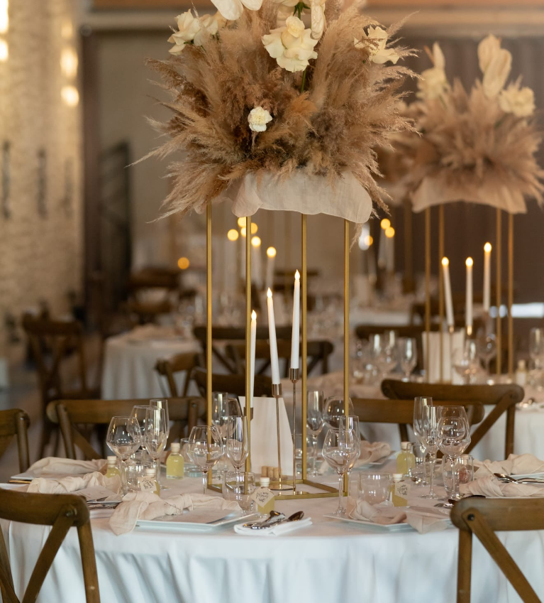 Dans la salle de réception du château de Roquefeuille, la décoration de table a été pensée comme une scénographie à part entière. Des centres de table floraux en hauteur, des bougies élancées et une vaisselle raffinée viennent sublimer l'espace.