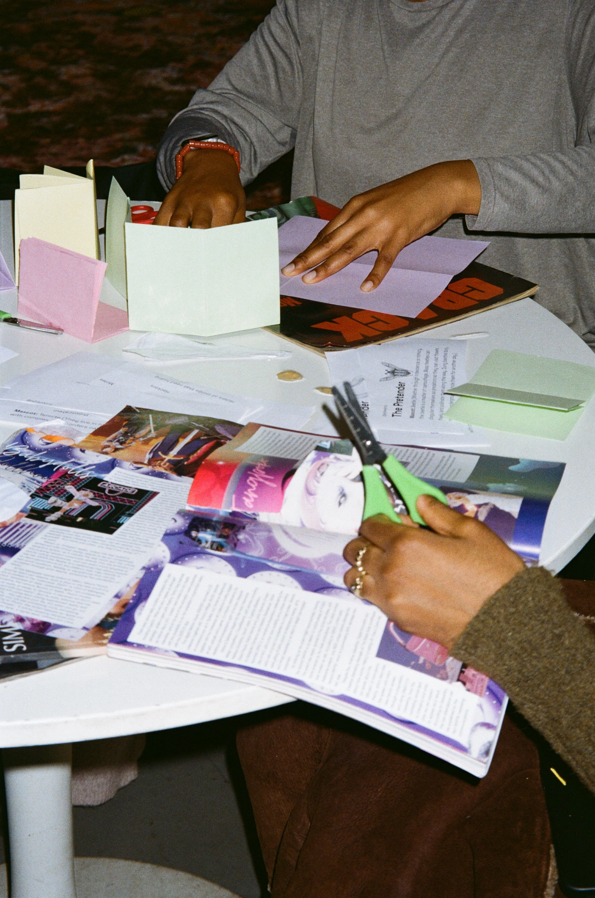 A close up image of a table with magazine cut outs, colourful paper and pens on it.