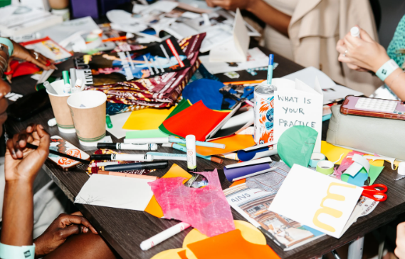 A close up image of a table with magazine cut outs, colourful paper and pens on it.