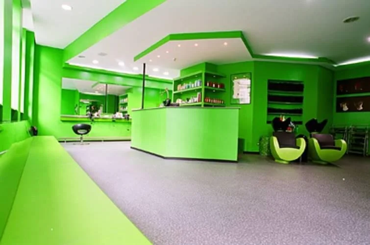 Heller, moderner Raum in leuchtend grün mit Bartheke, schwarzen Barhockern und bequemen schwarzen und grünen Sesseln, wohl eine Lounge oder ein Café.