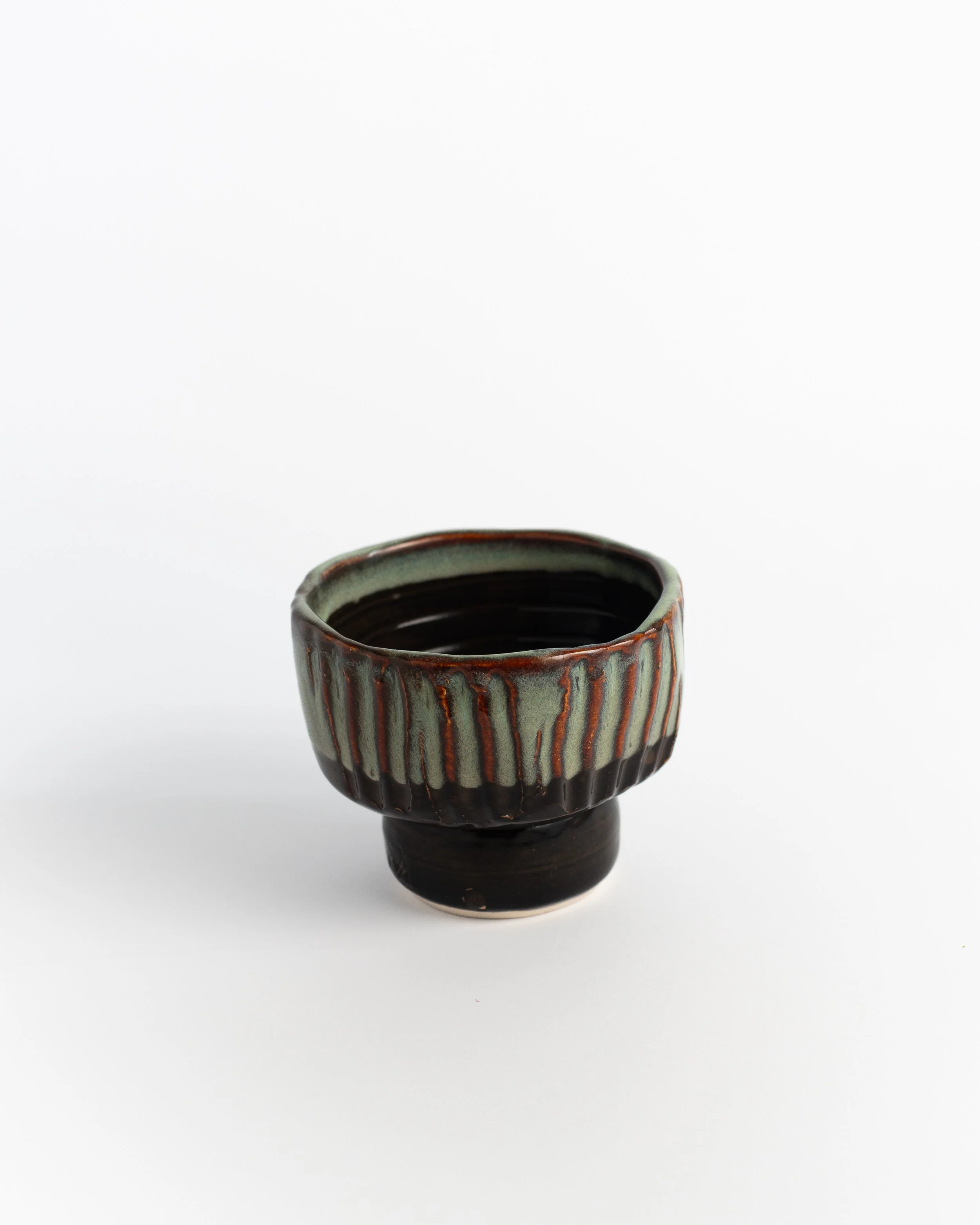 Footed ceramic ice cream bowl with carved vertical flutes in dark brown glaze breaking to pale green.