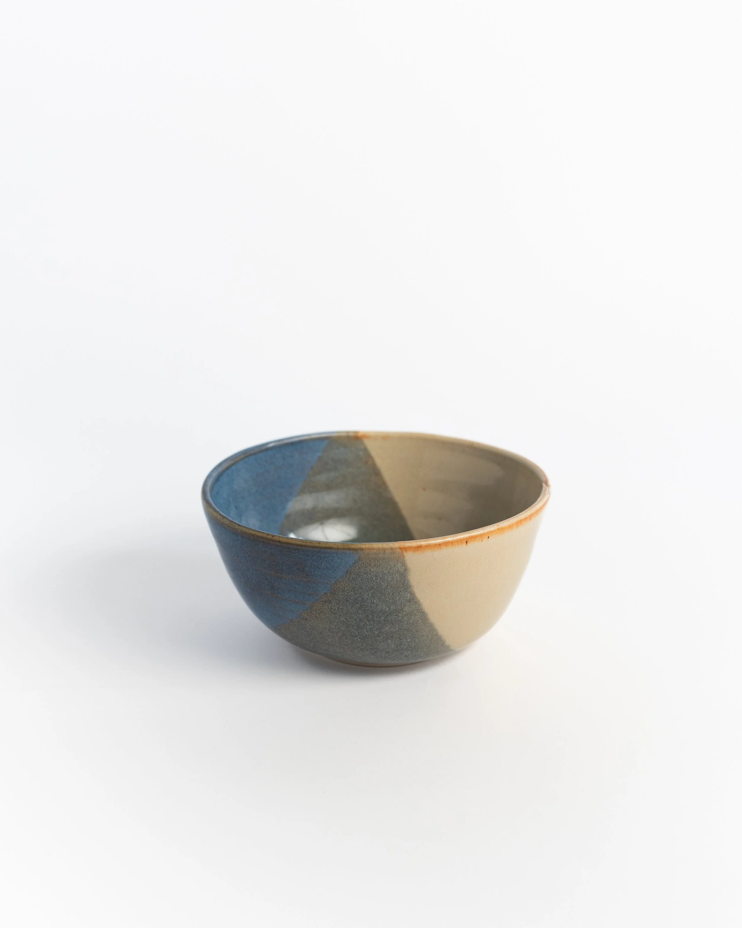 Rounded ceramic bowl where slate blue meets a wedge of warm sand, finished with a soft amber rim.