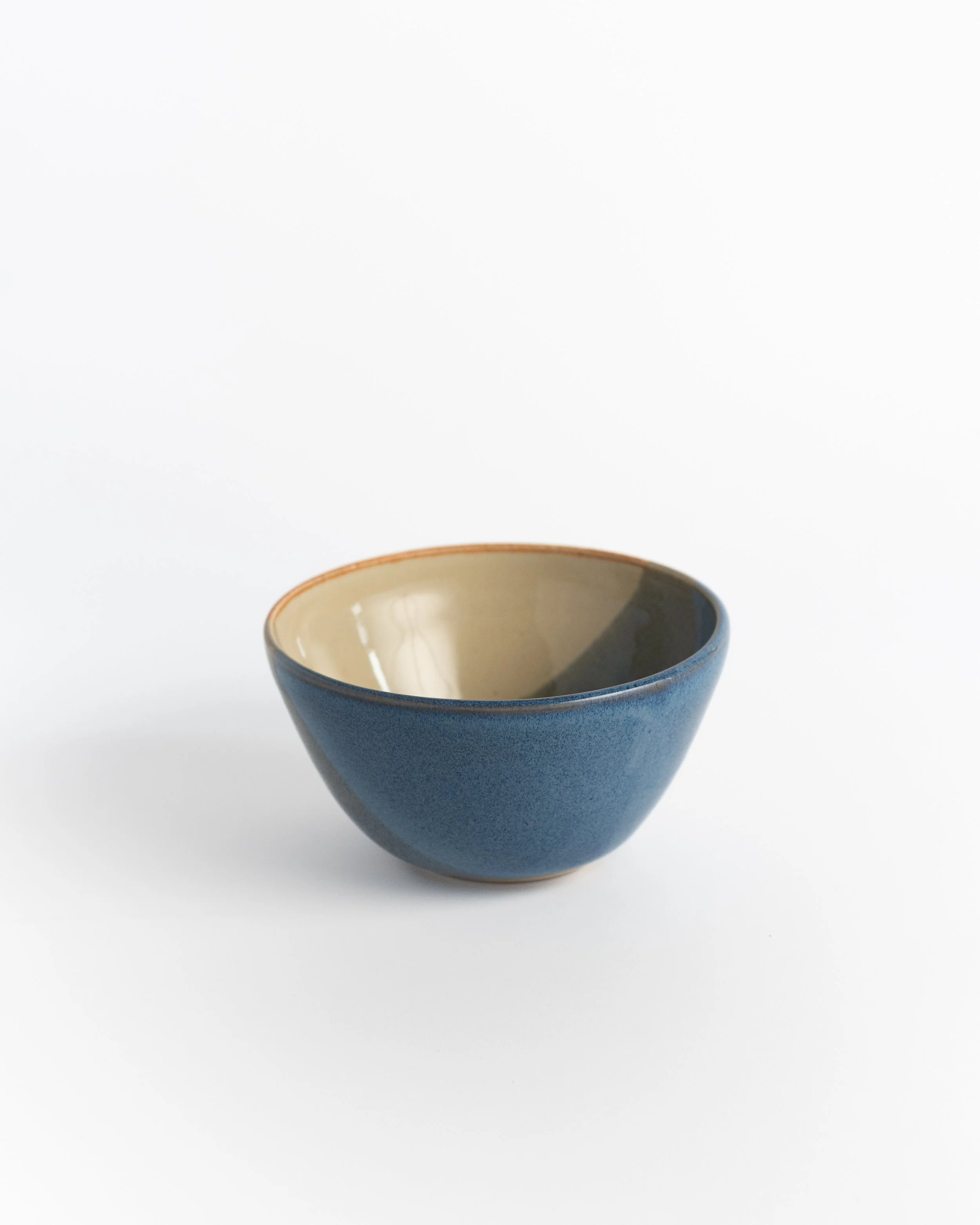 Rounded ceramic bowl in slate blue with a creamy interior that pools with light.