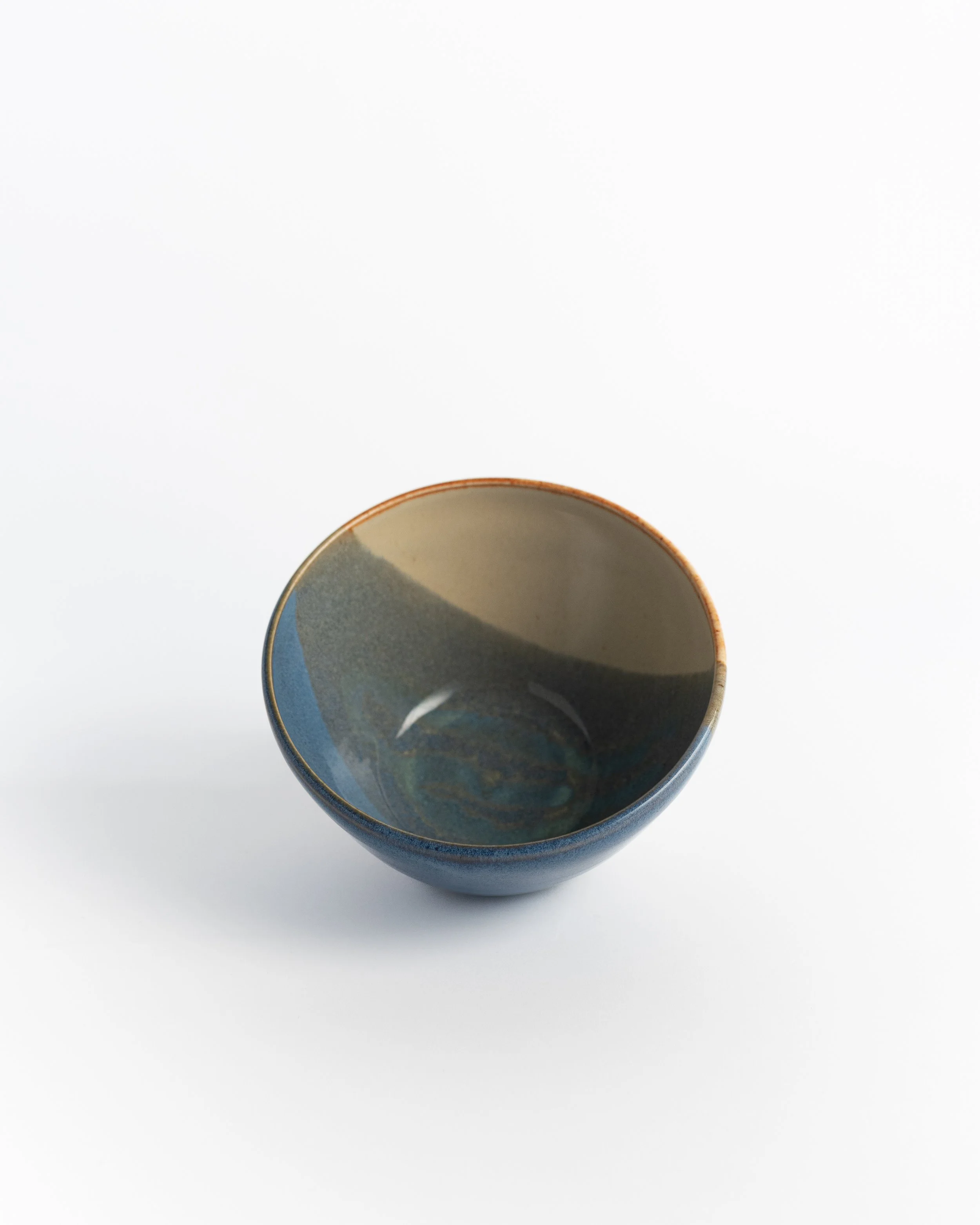 Rounded slate blue ceramic bowl seen from above, dark and cream glaze split across the well.
