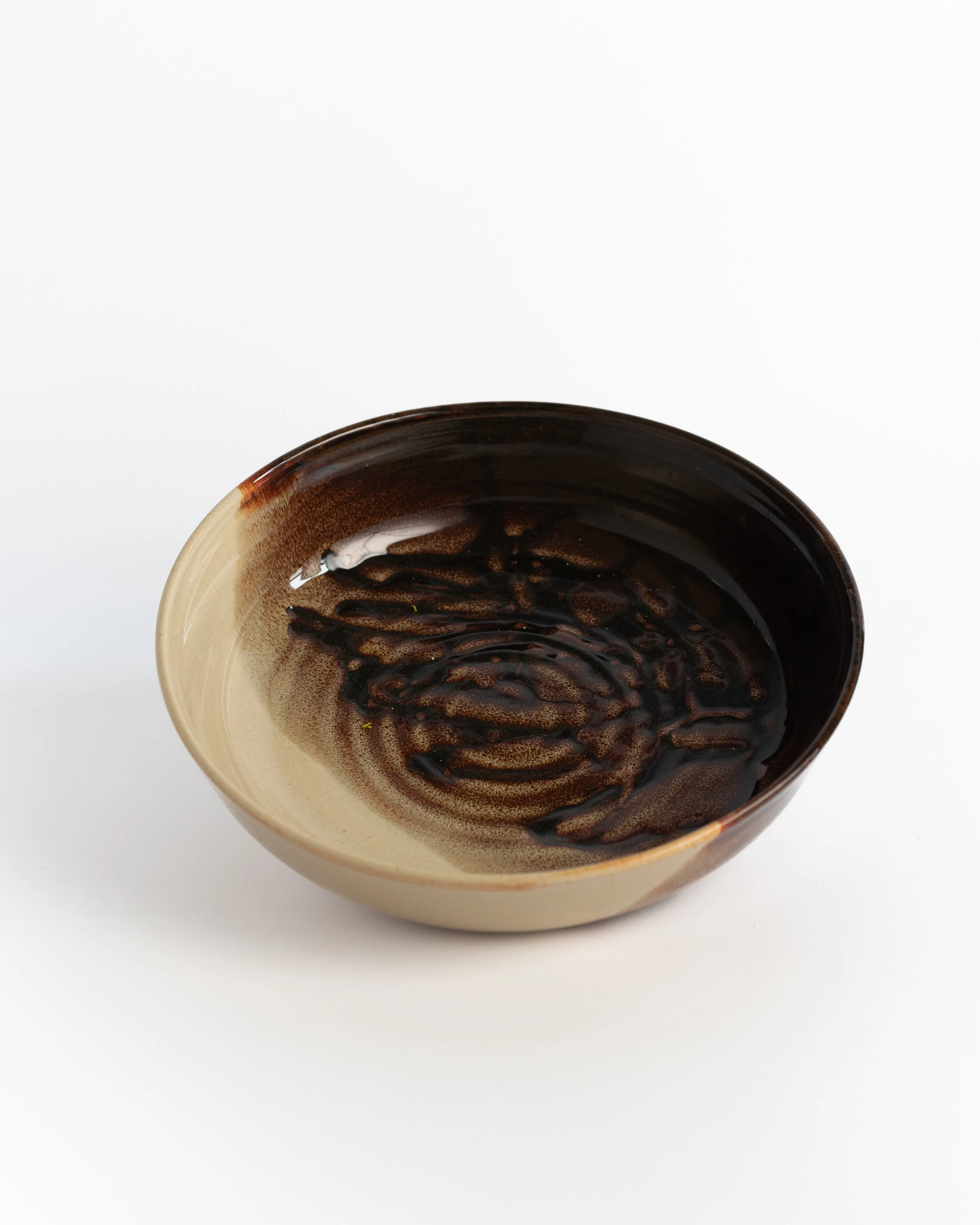 Deep ceramic serving bowl in warm cream with glossy tortoiseshell brown swirling across the well.