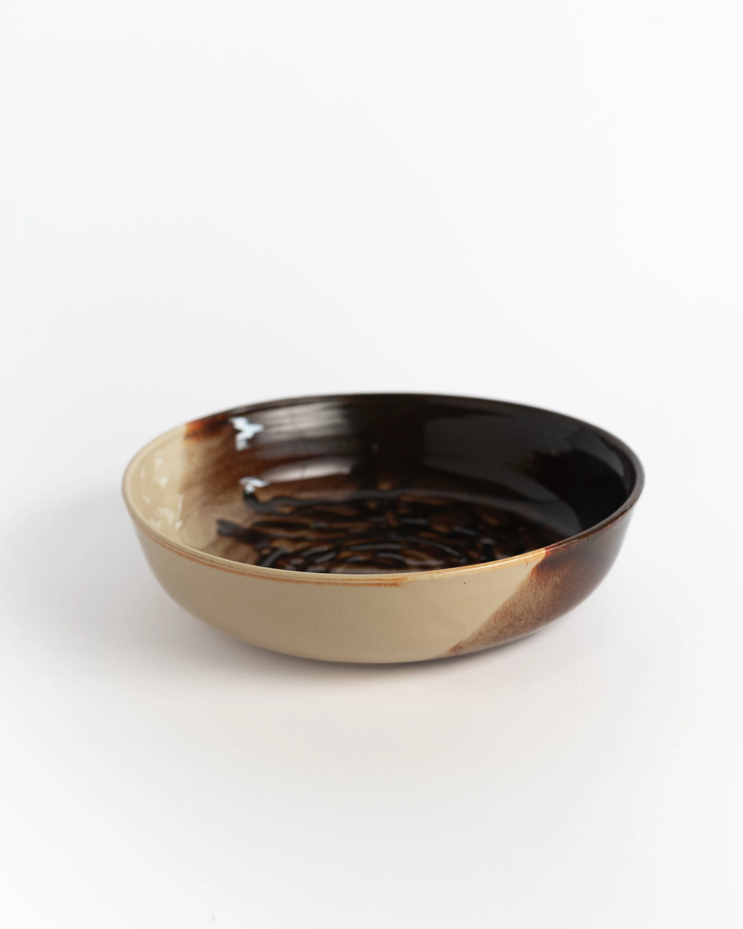 Cream and brown ceramic serving bowl seen from a low angle, glaze pooling toward the center.