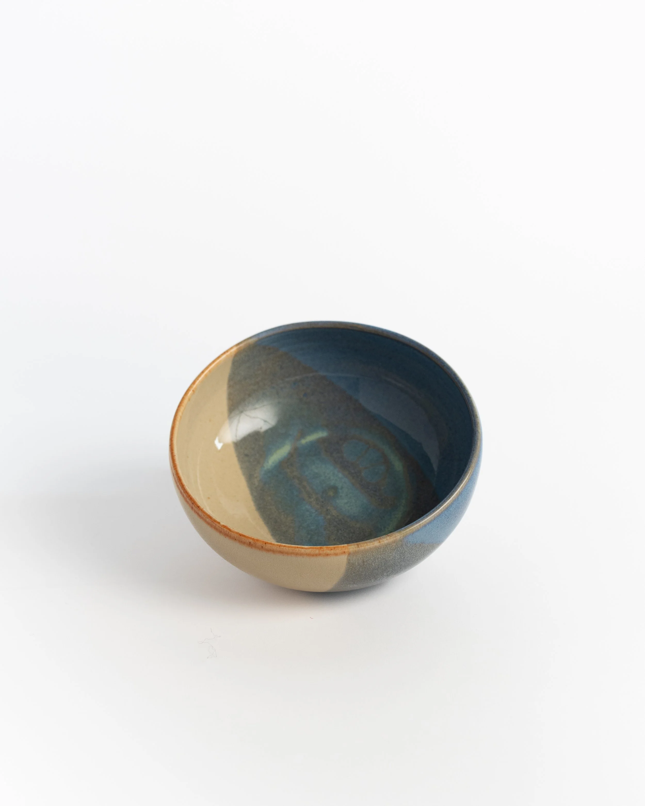 Wide shallow ceramic bowl in slate blue with a warm sand wedge and a soft amber rim.