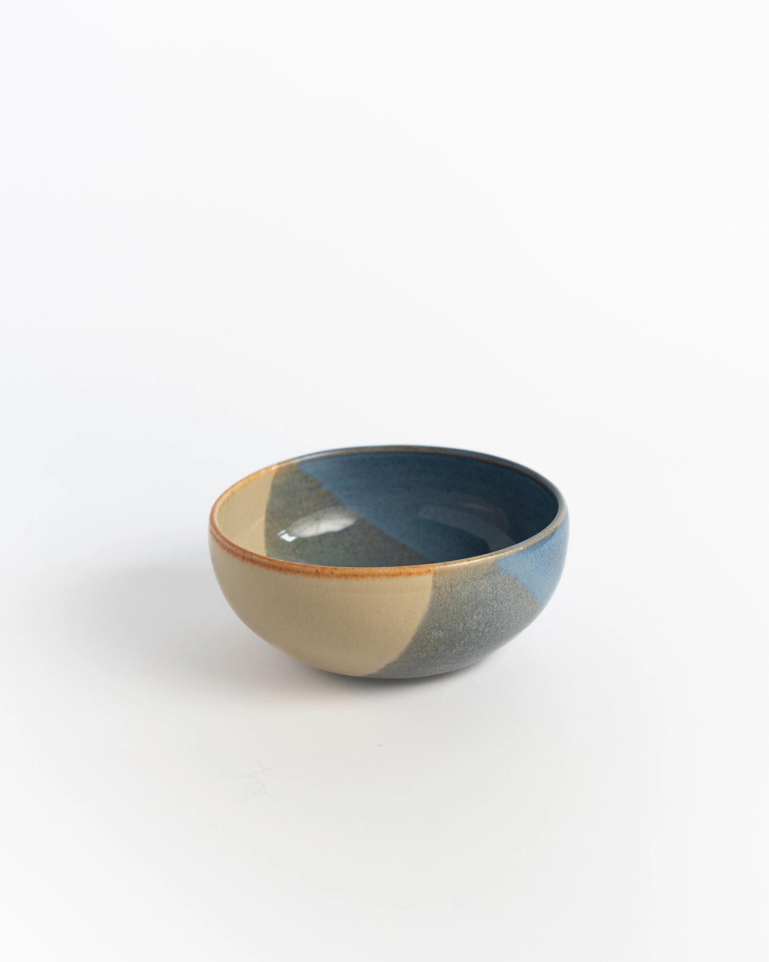 Wide slate blue ceramic bowl seen from the side, sand-toned glaze wrapping the exterior.