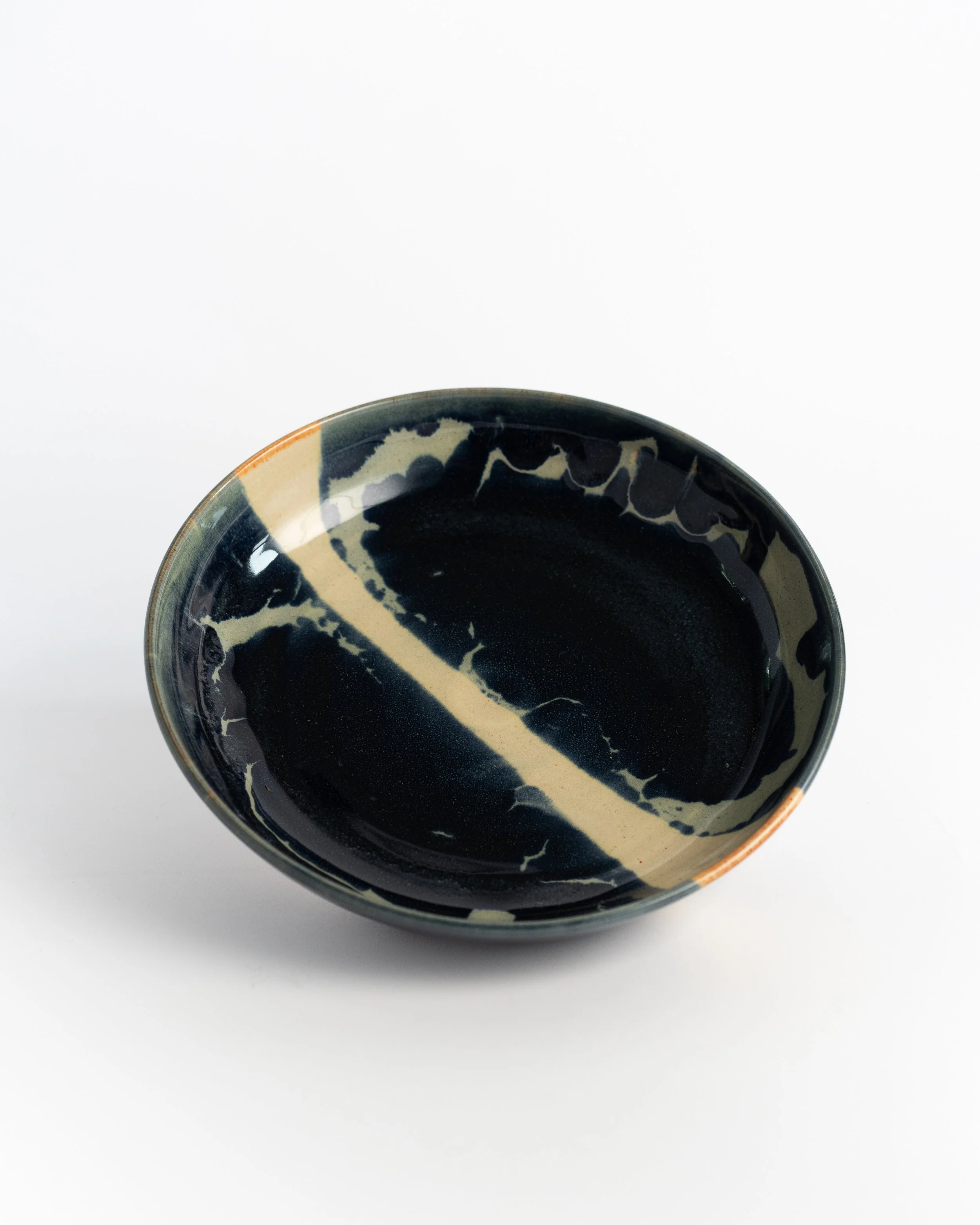 Shallow ceramic bowl in deep midnight glaze with a pale streak arcing across the surface.