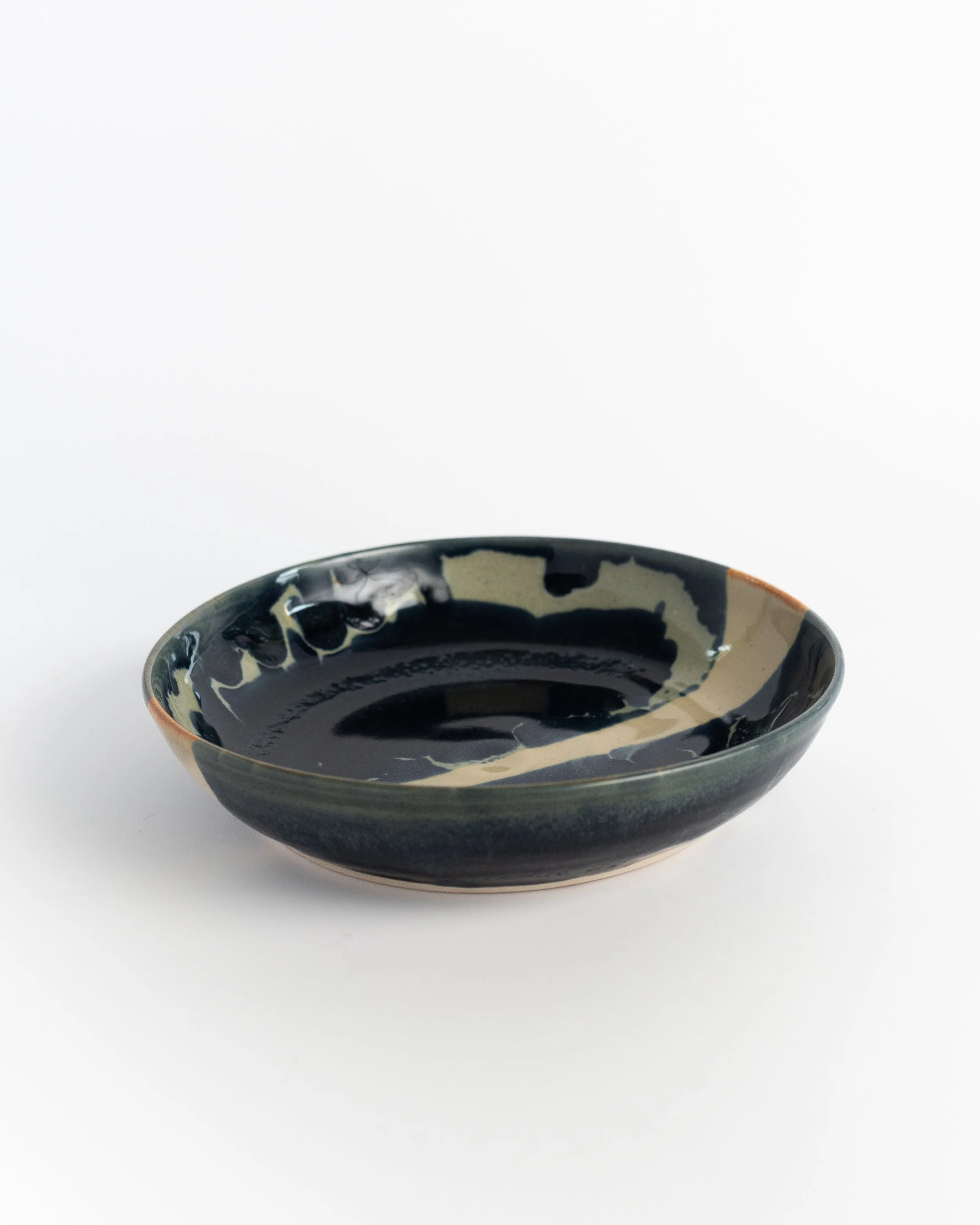 Shallow midnight ceramic bowl seen from the side, pale glaze breaking across the dark rim.