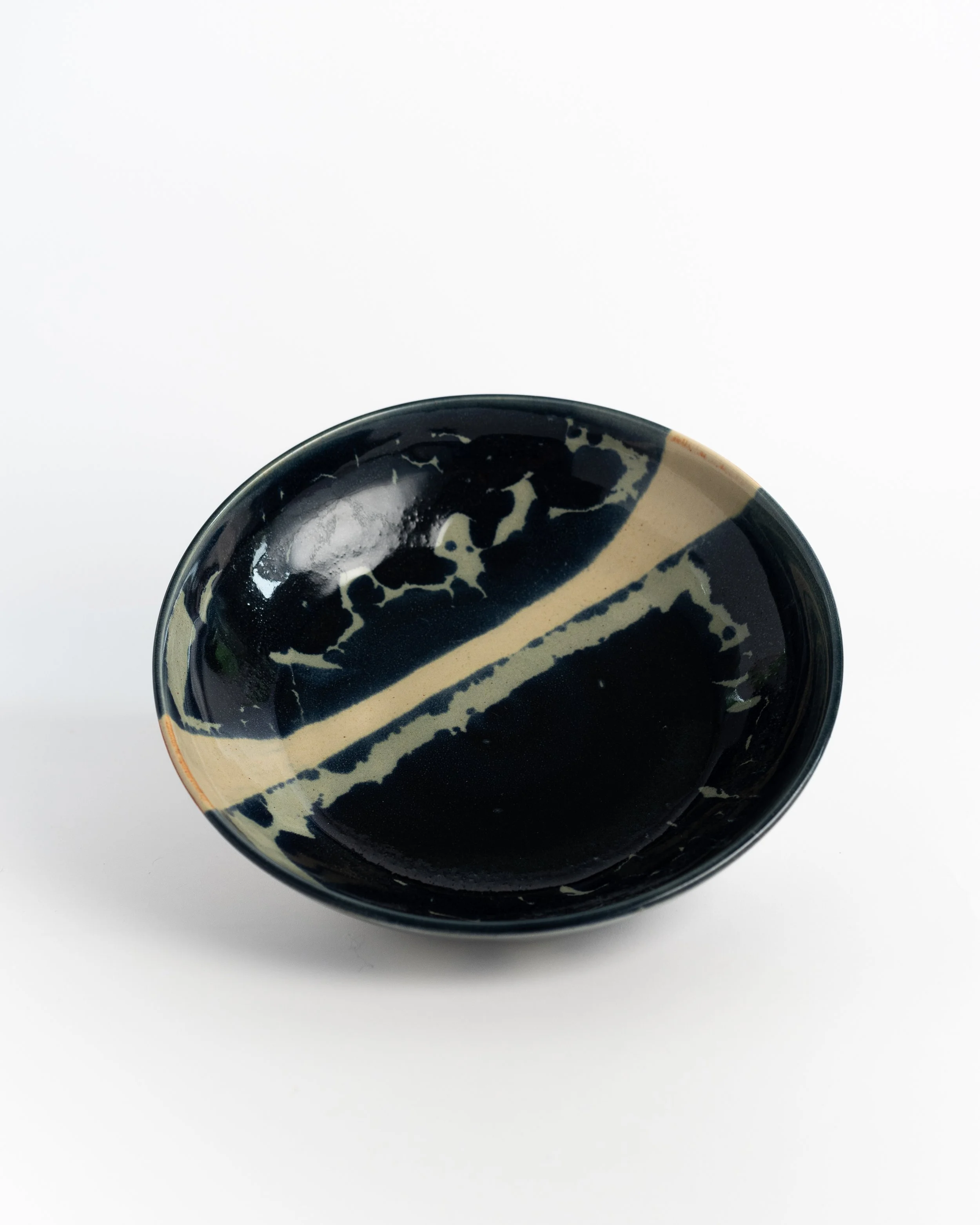 Shallow ceramic bowl in deep midnight glaze with a pale streak arcing across the surface.