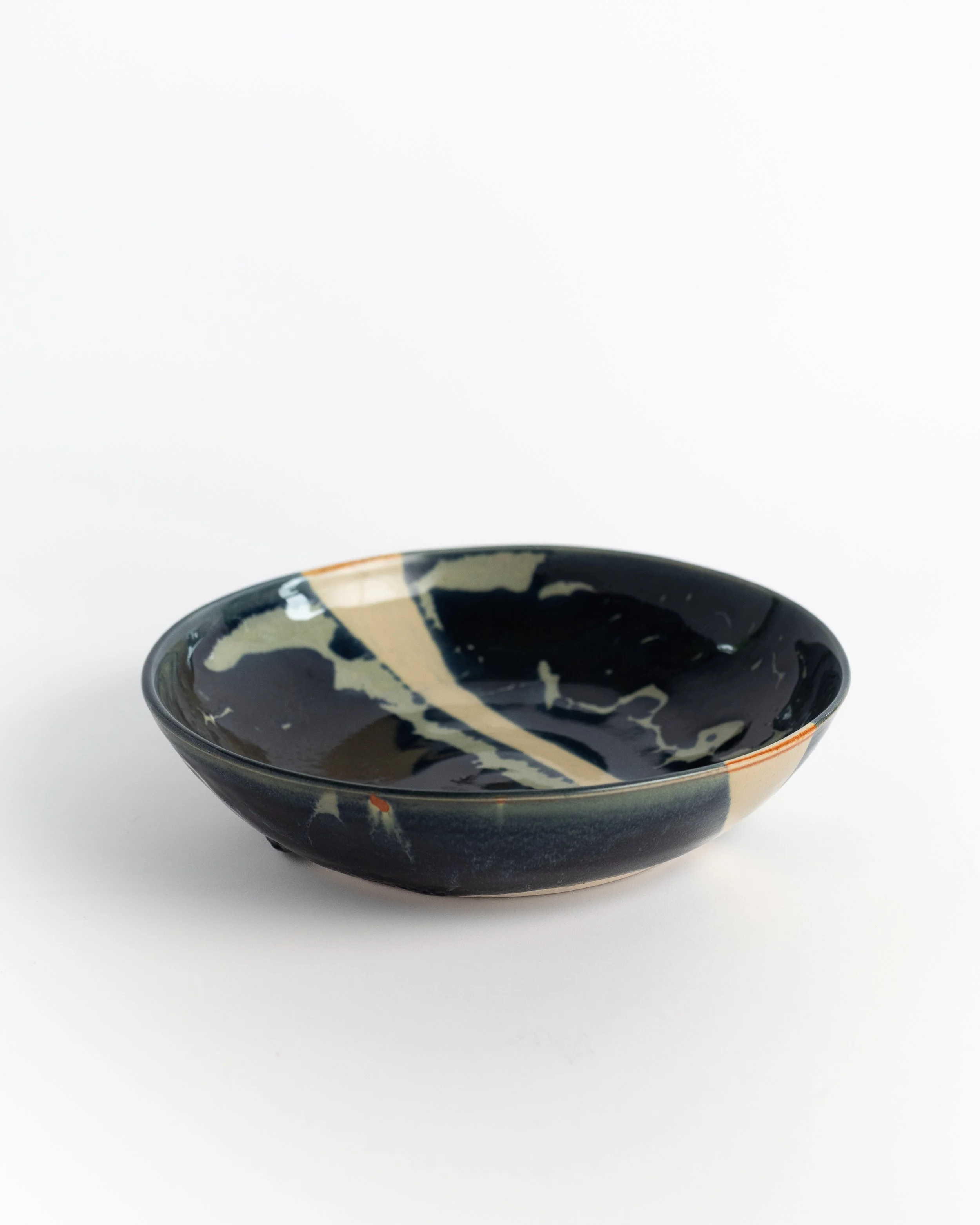 Shallow midnight ceramic bowl seen from the side, pale glaze breaking across the dark rim.