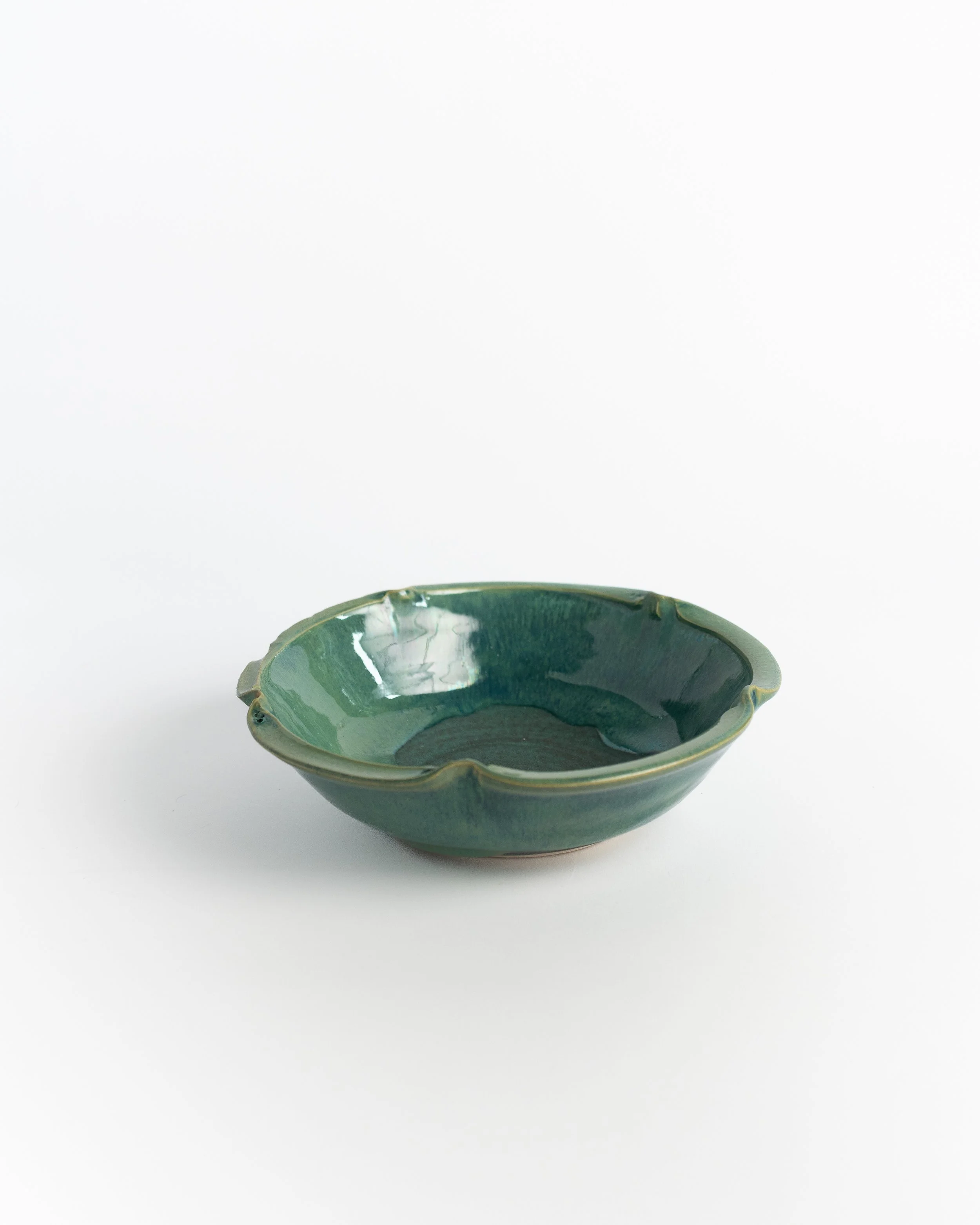 Softly scalloped ceramic bowl in deep glossy green with petal-shaped edges.