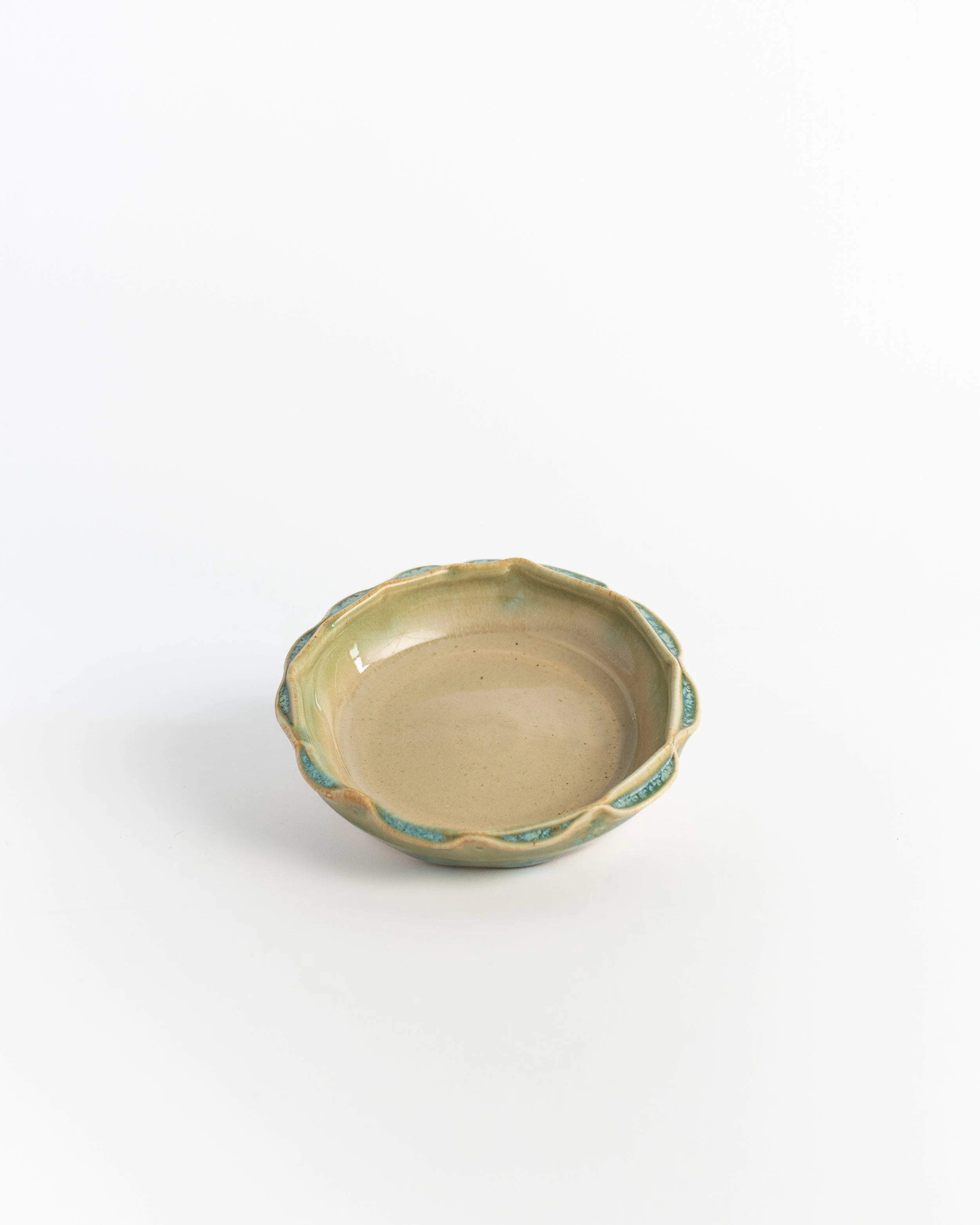 Small shallow ceramic dish in warm cream with a rippling green rim.
