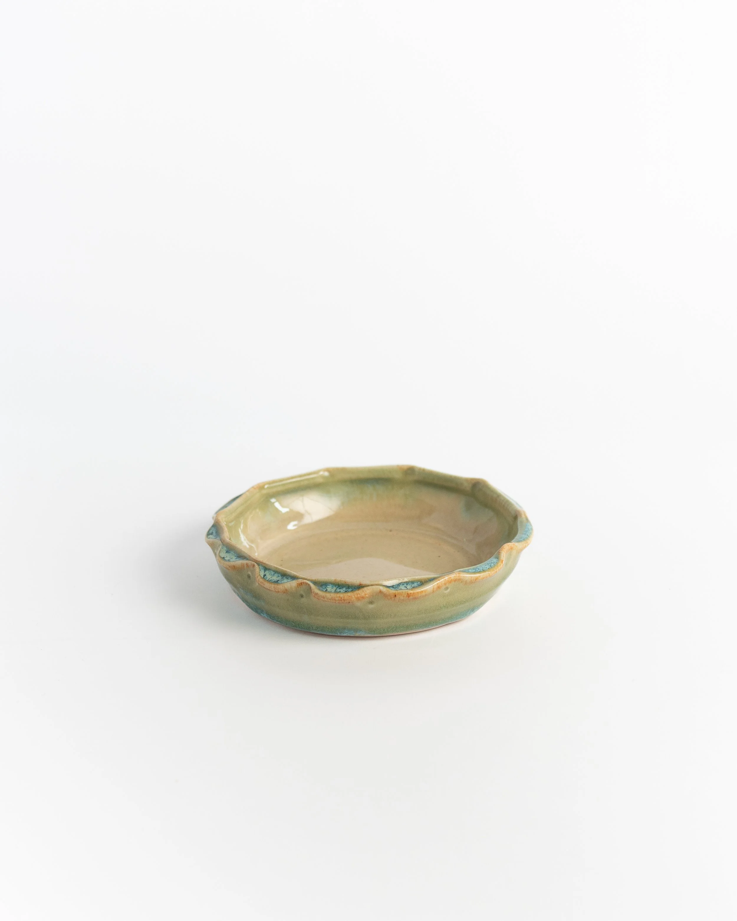 Small cream ceramic dish seen from a low angle, green glaze breaking along the wavy rim.