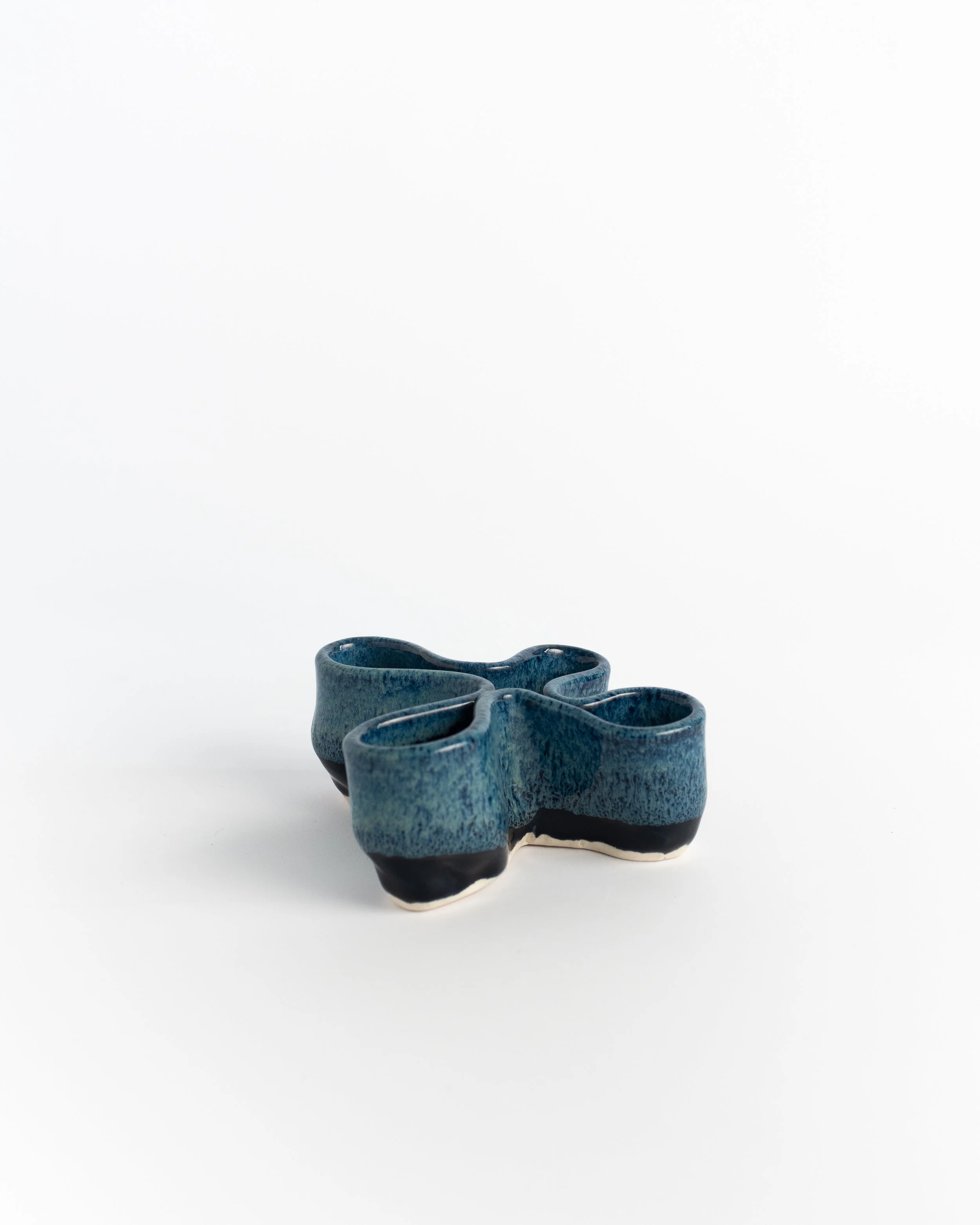 Low three-lobed ceramic dish in mottled teal with black and cream edges.
