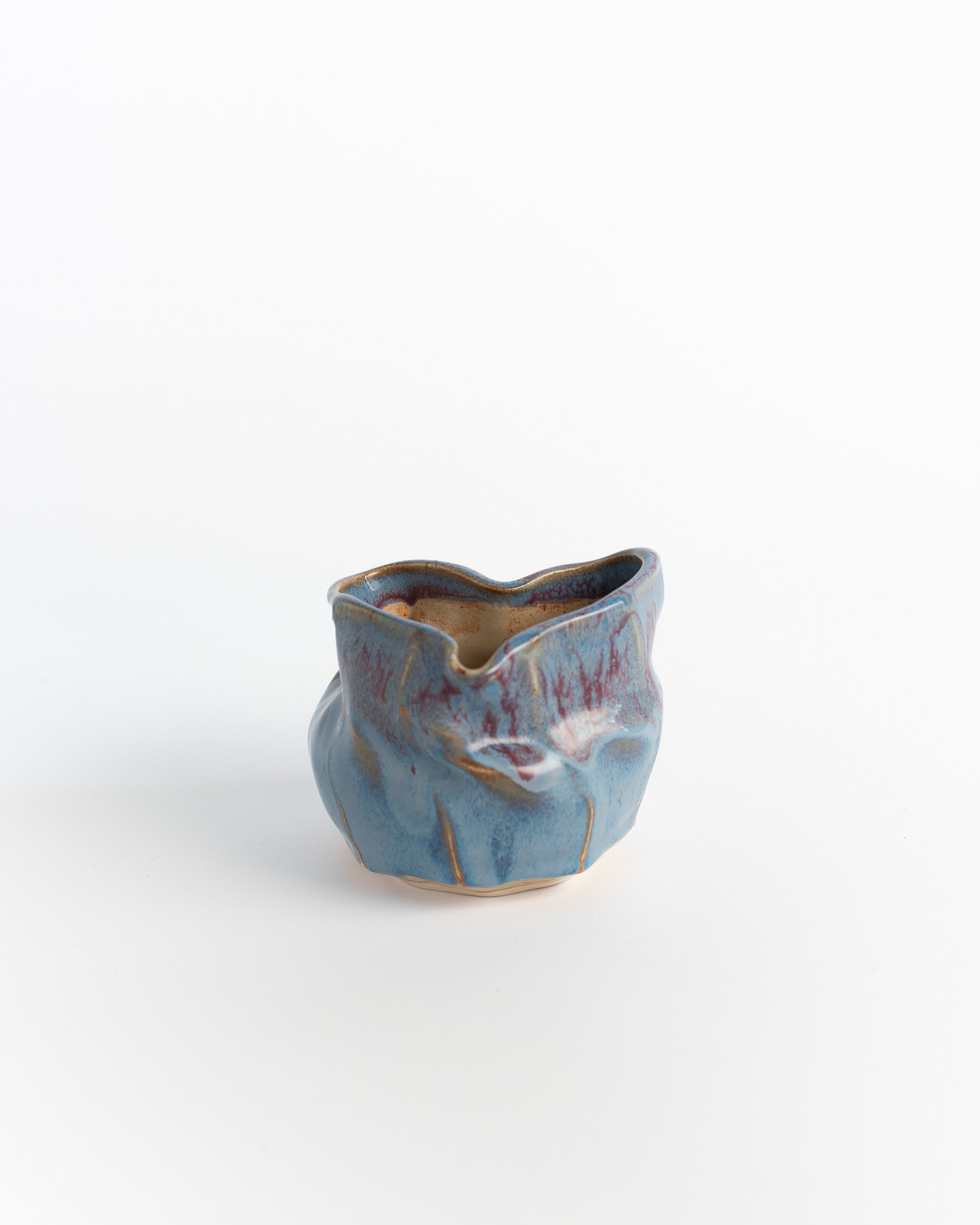 Sculptural pinched ceramic vessel in drifting blue and lavender with softly folded walls.