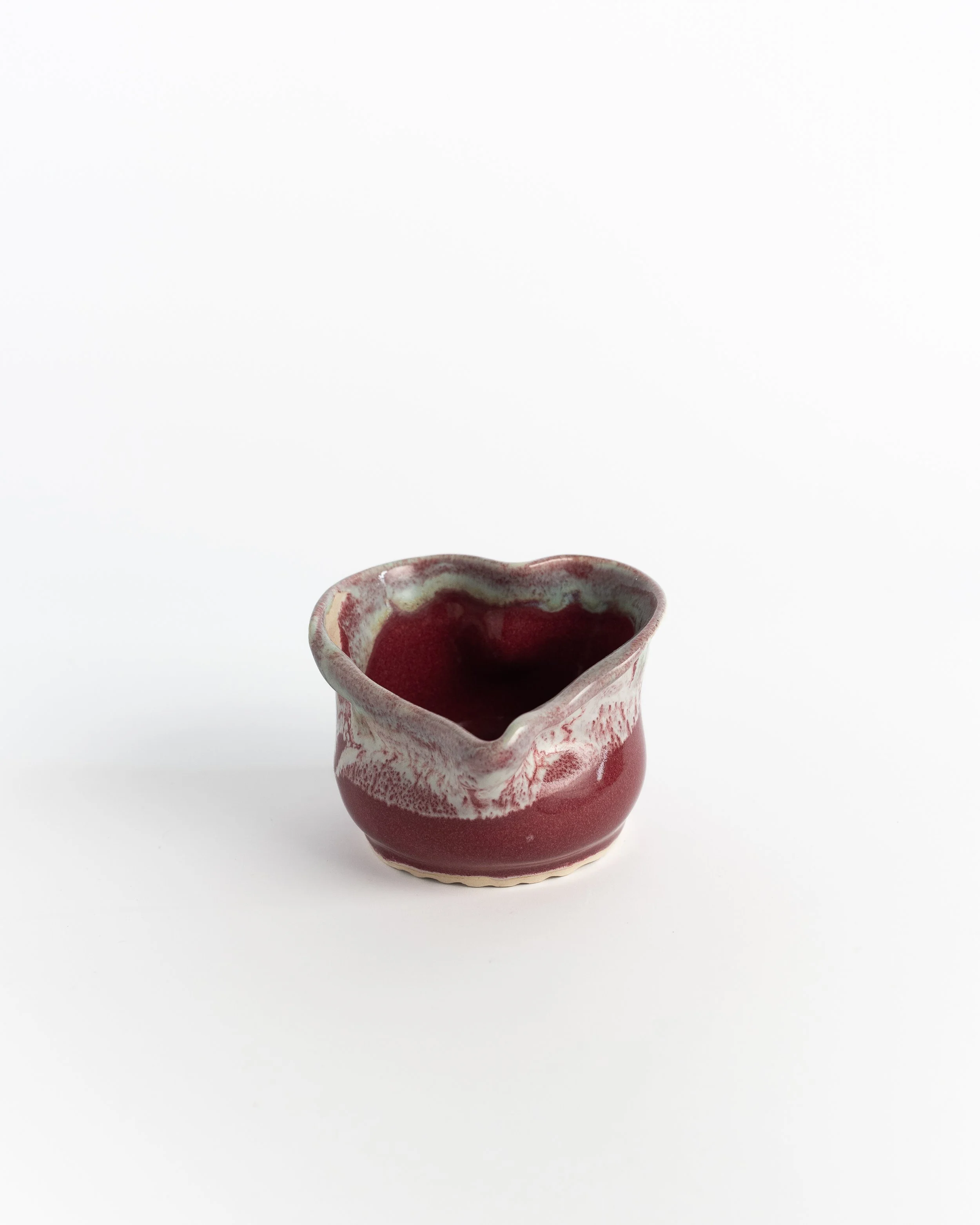 Sculptural pinched ceramic bowl in deep crimson with frosted white folds at the rim.