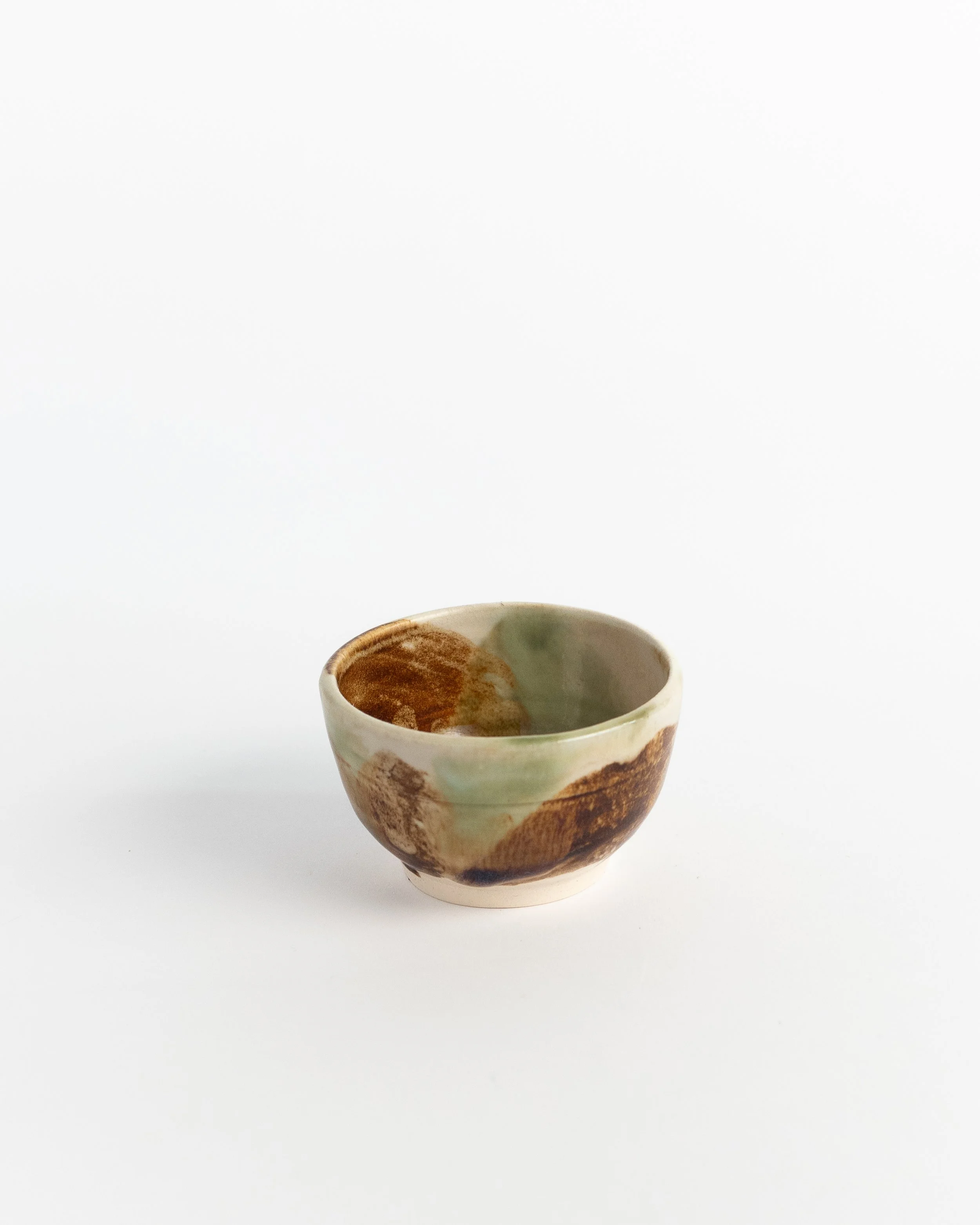 Small ceramic bowl in pale green washed with amber and rust across the walls.