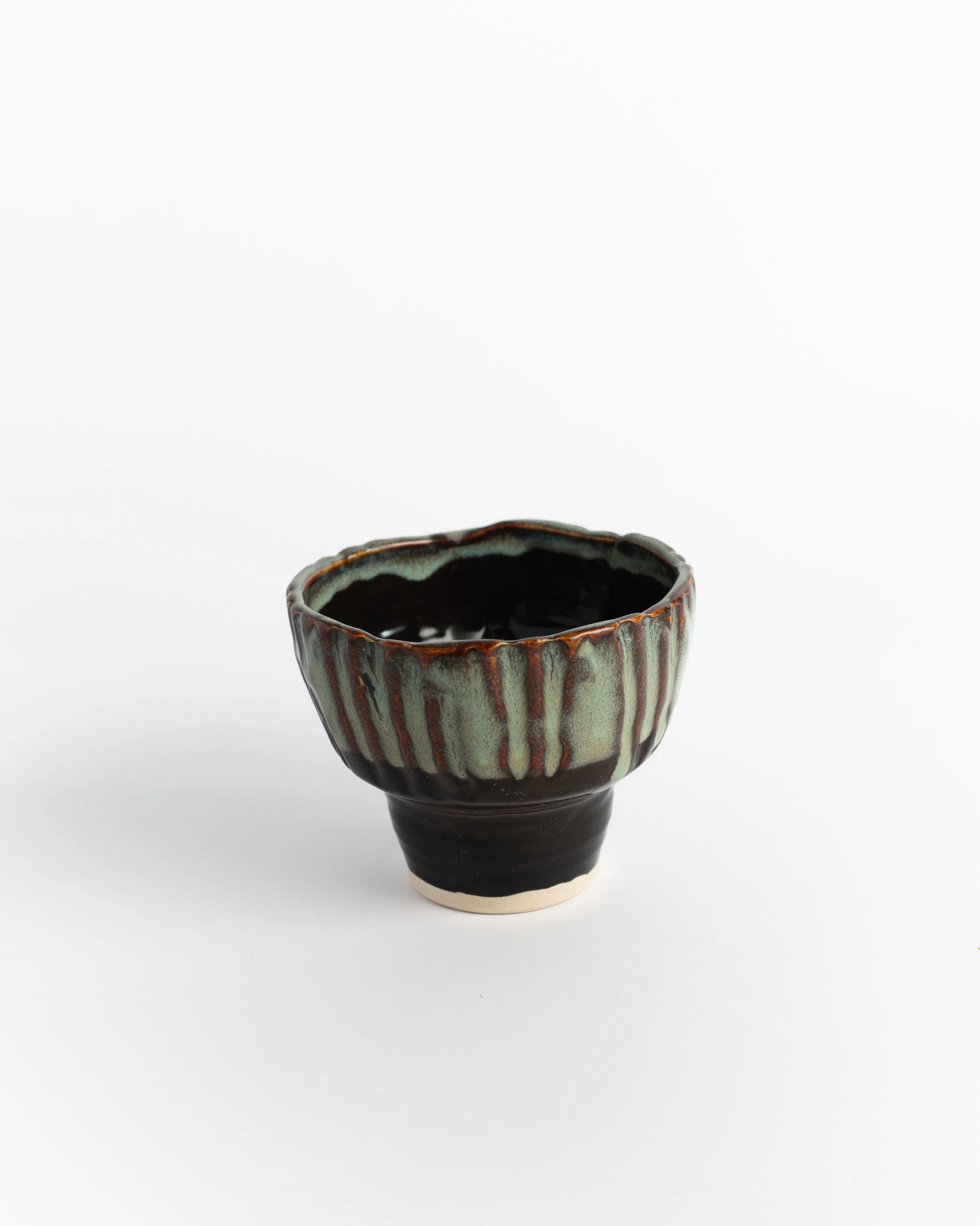 Footed ceramic ice cream bowl with carved vertical flutes in dark brown glaze breaking to pale green.