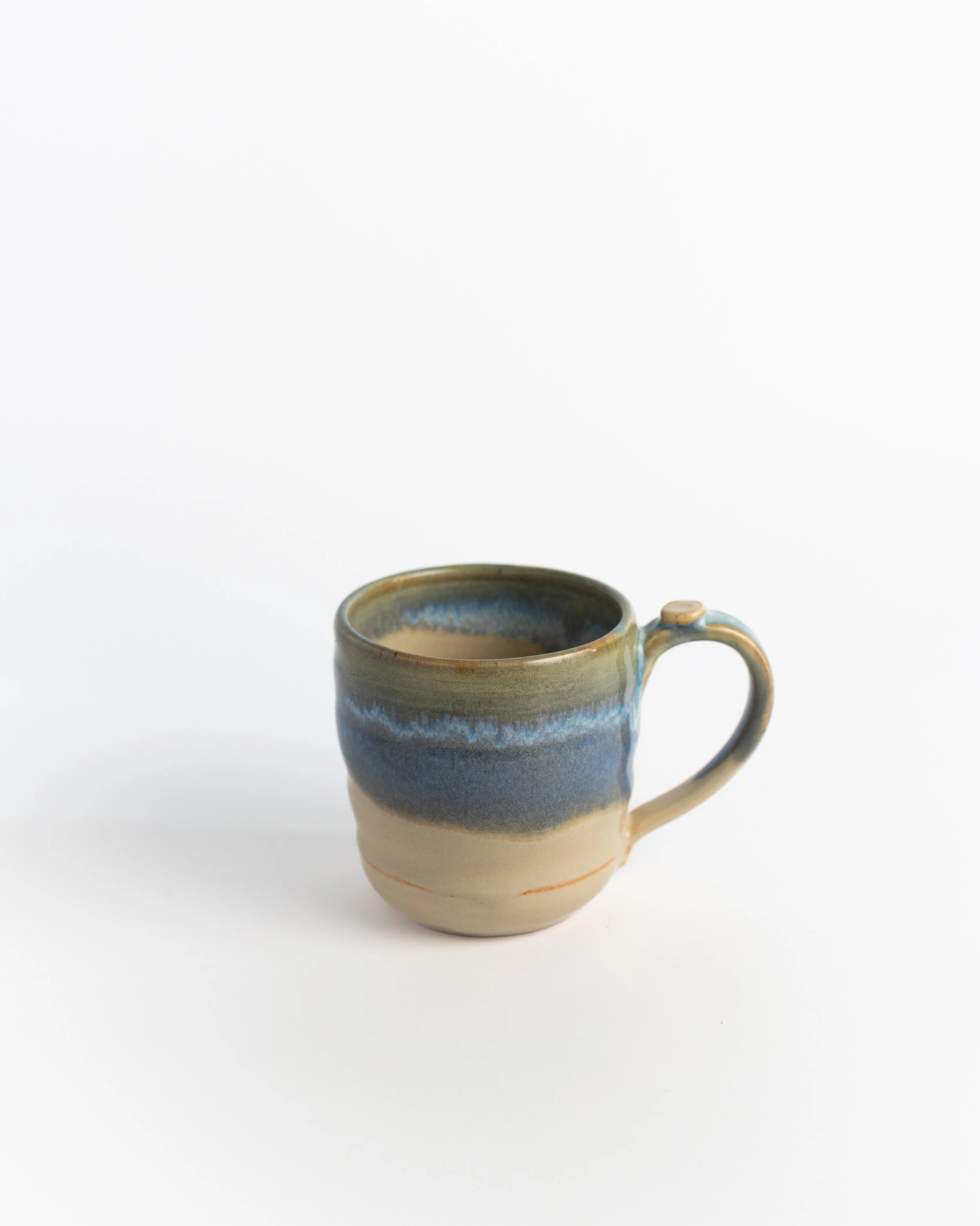 Ceramic mug in natural sand clay with a band of blue and green washing across the middle.