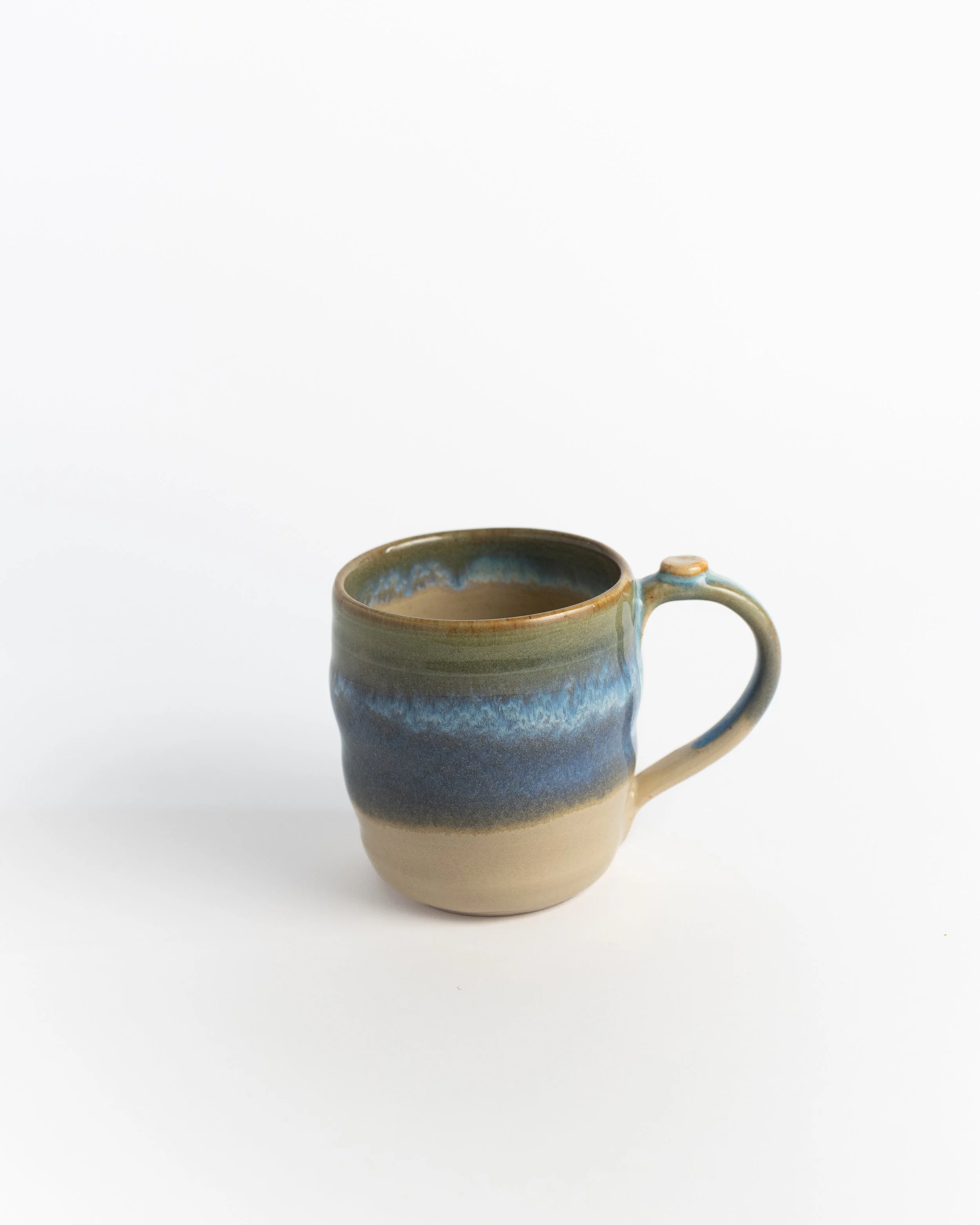 Ceramic mug in natural sand clay with a band of blue and green washing across the middle.