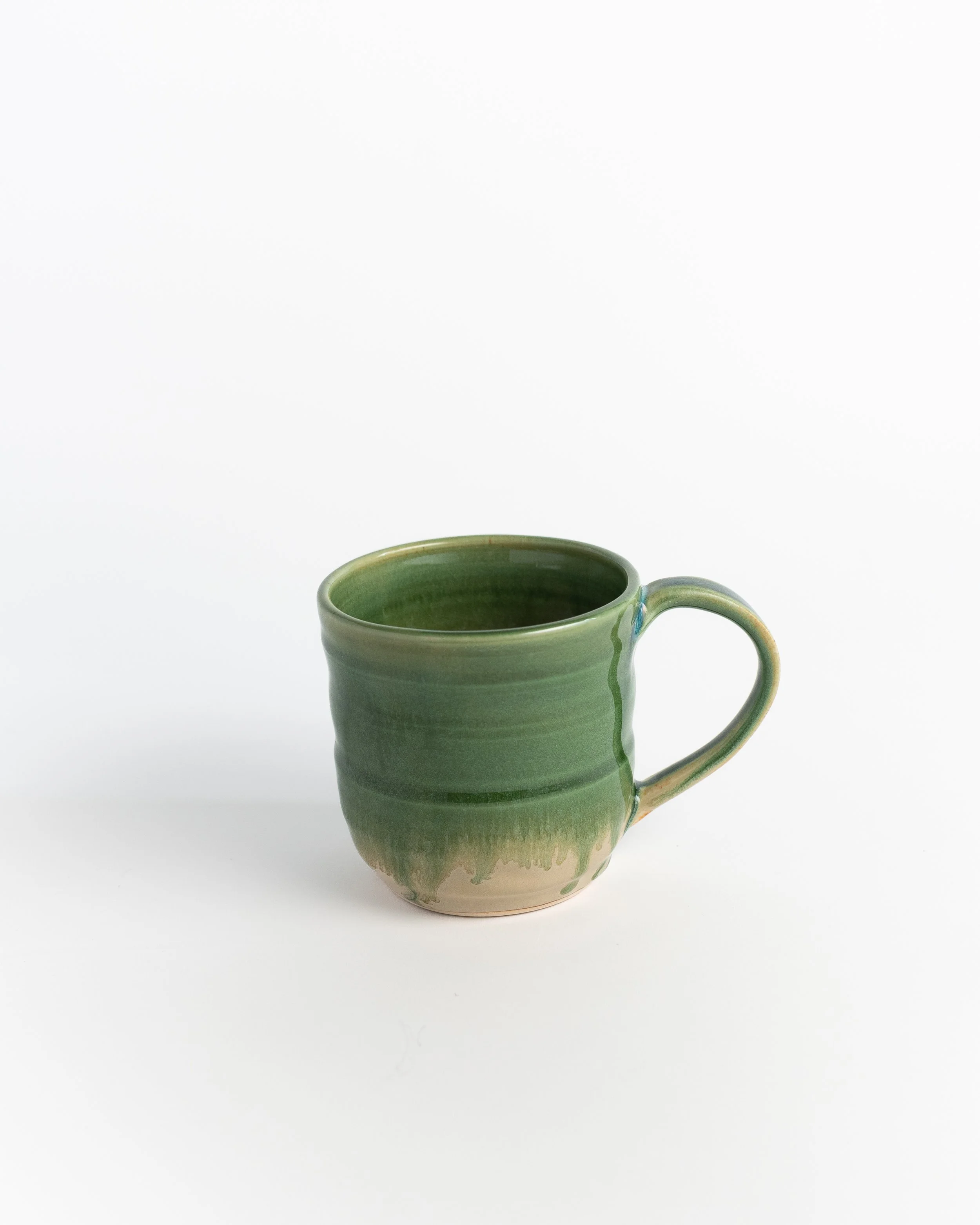 Ceramic mug in glossy spring green fading to bare clay at the foot.