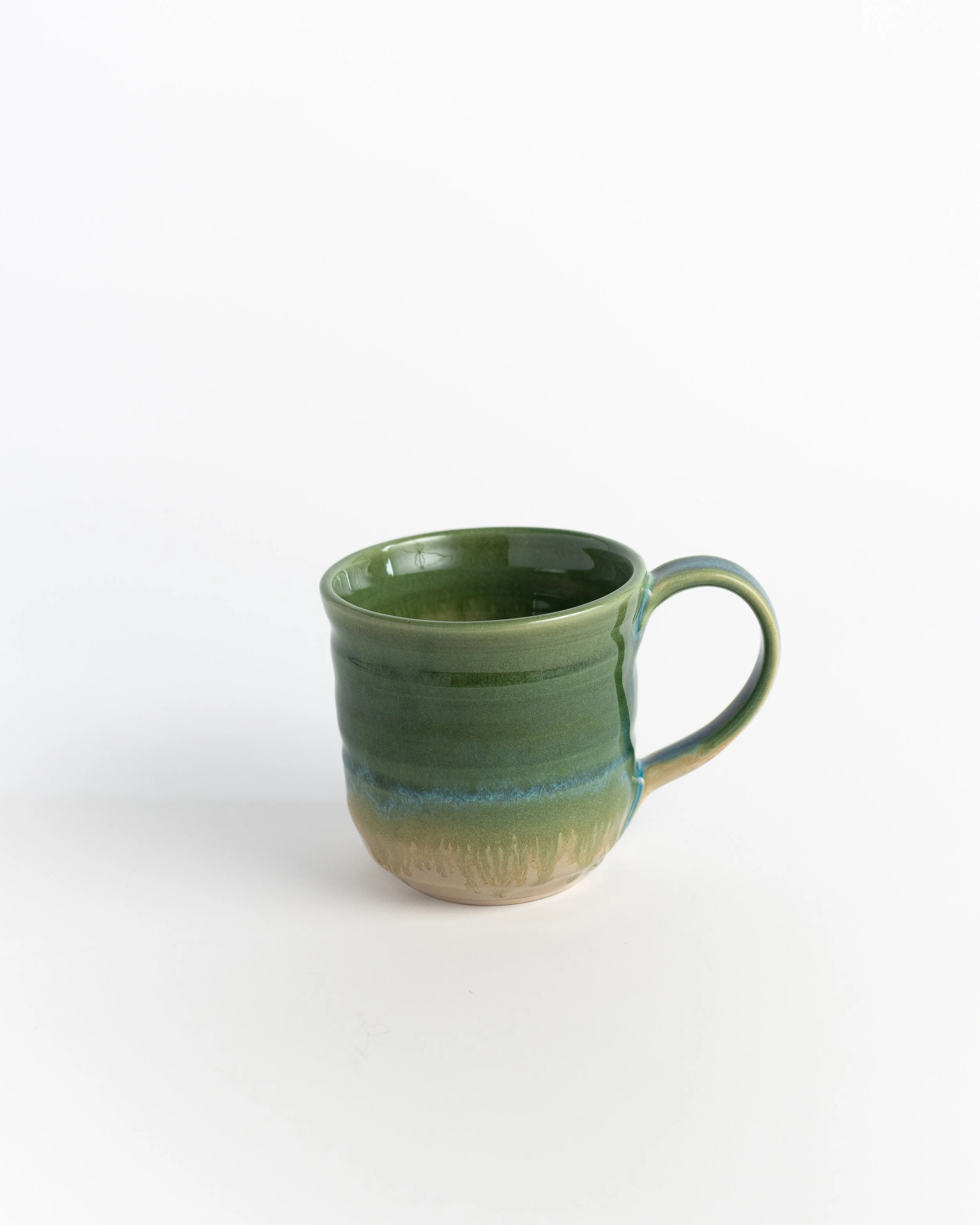 Ceramic mug in glossy spring green with a thread of turquoise pooling near the base.