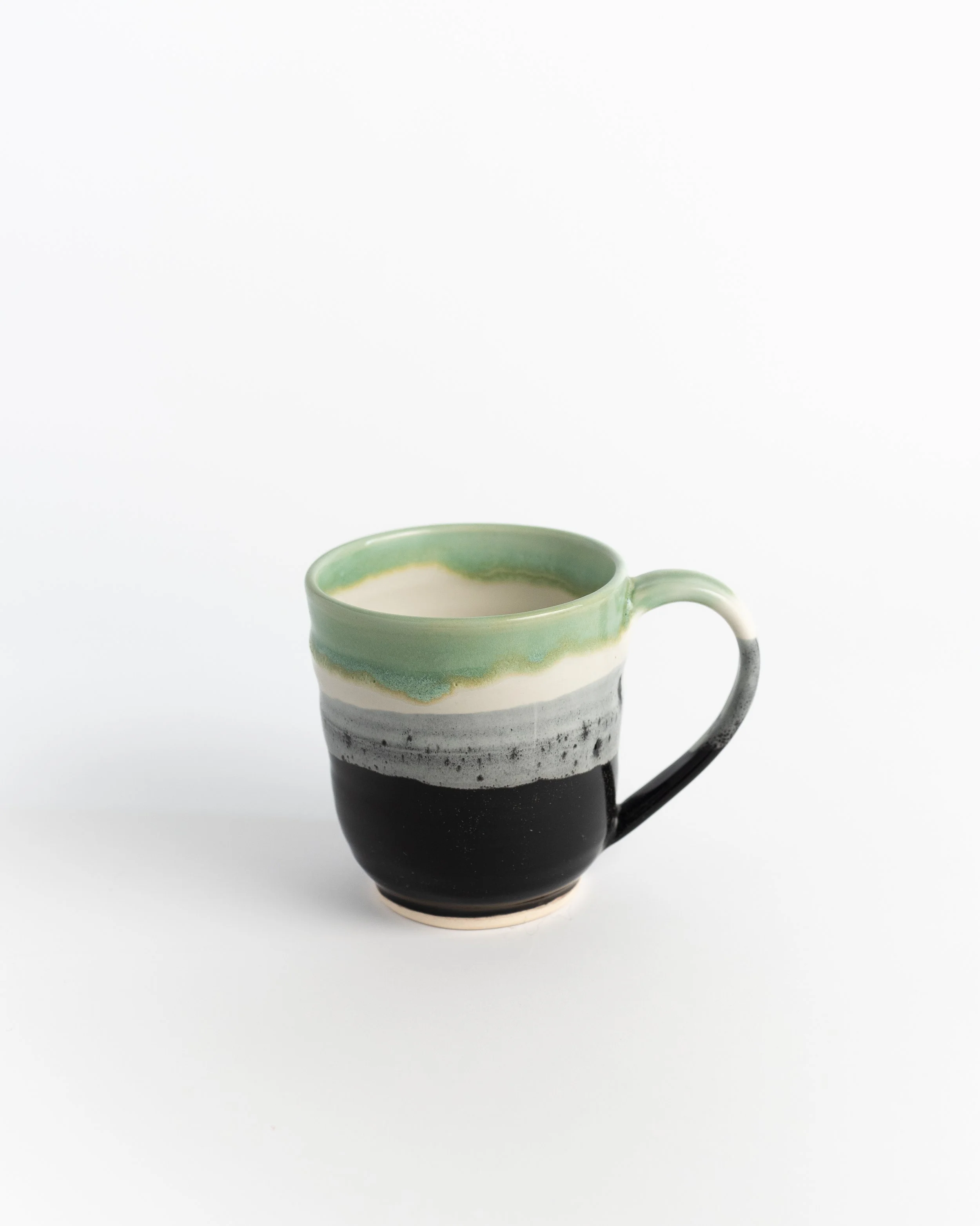 Ceramic mug layered from dark earth through a speckled snow band to soft green at the rim.