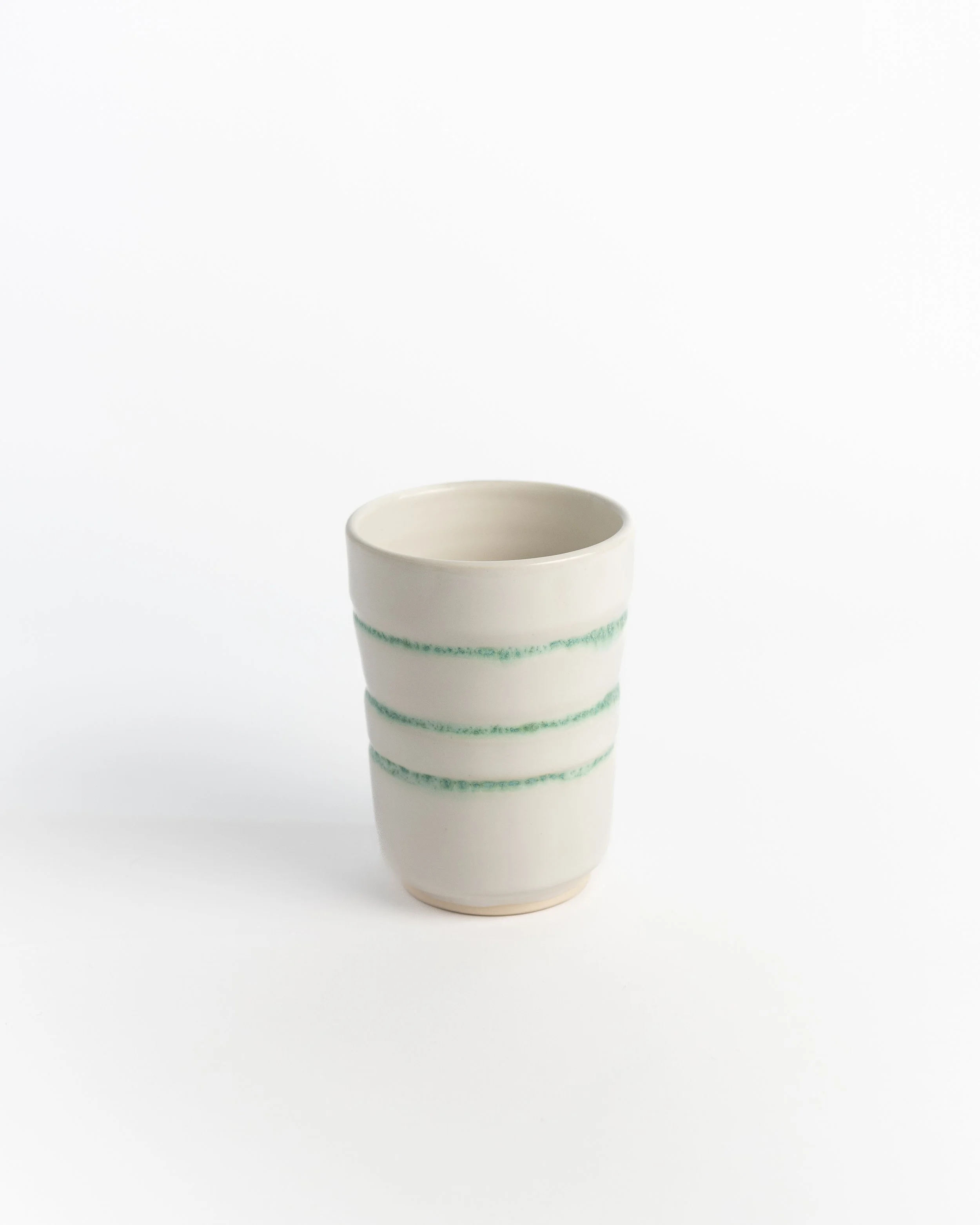 Handleless ceramic tumbler in creamy white wrapped with three loose bands of green.