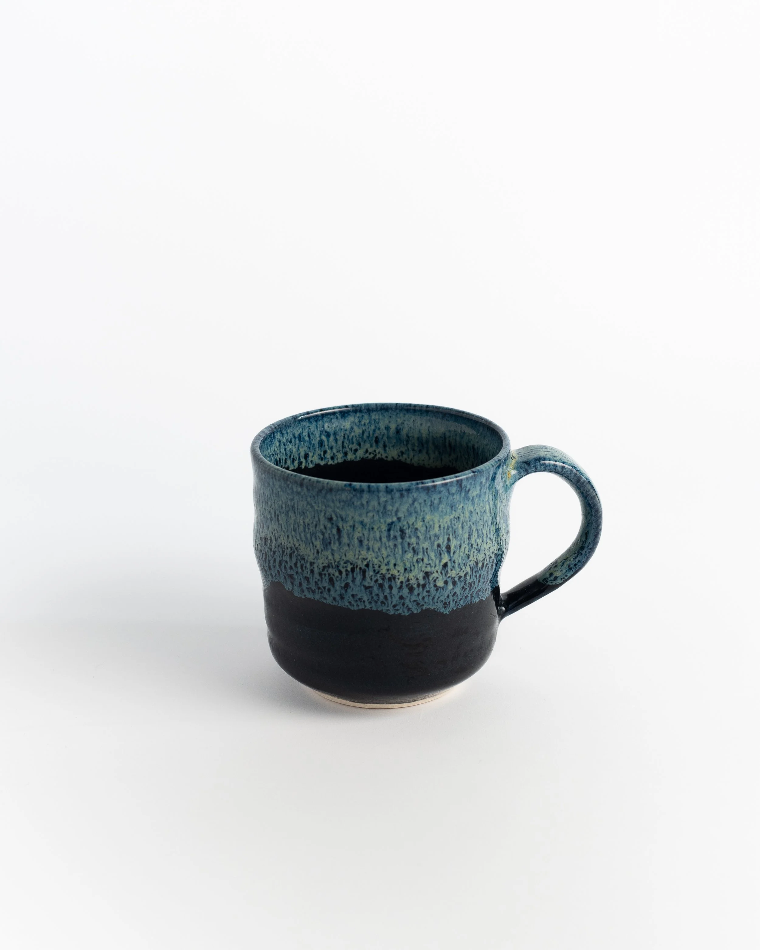 Ceramic mug in matte black rising into a mottled teal band, with a rich teal interior.
