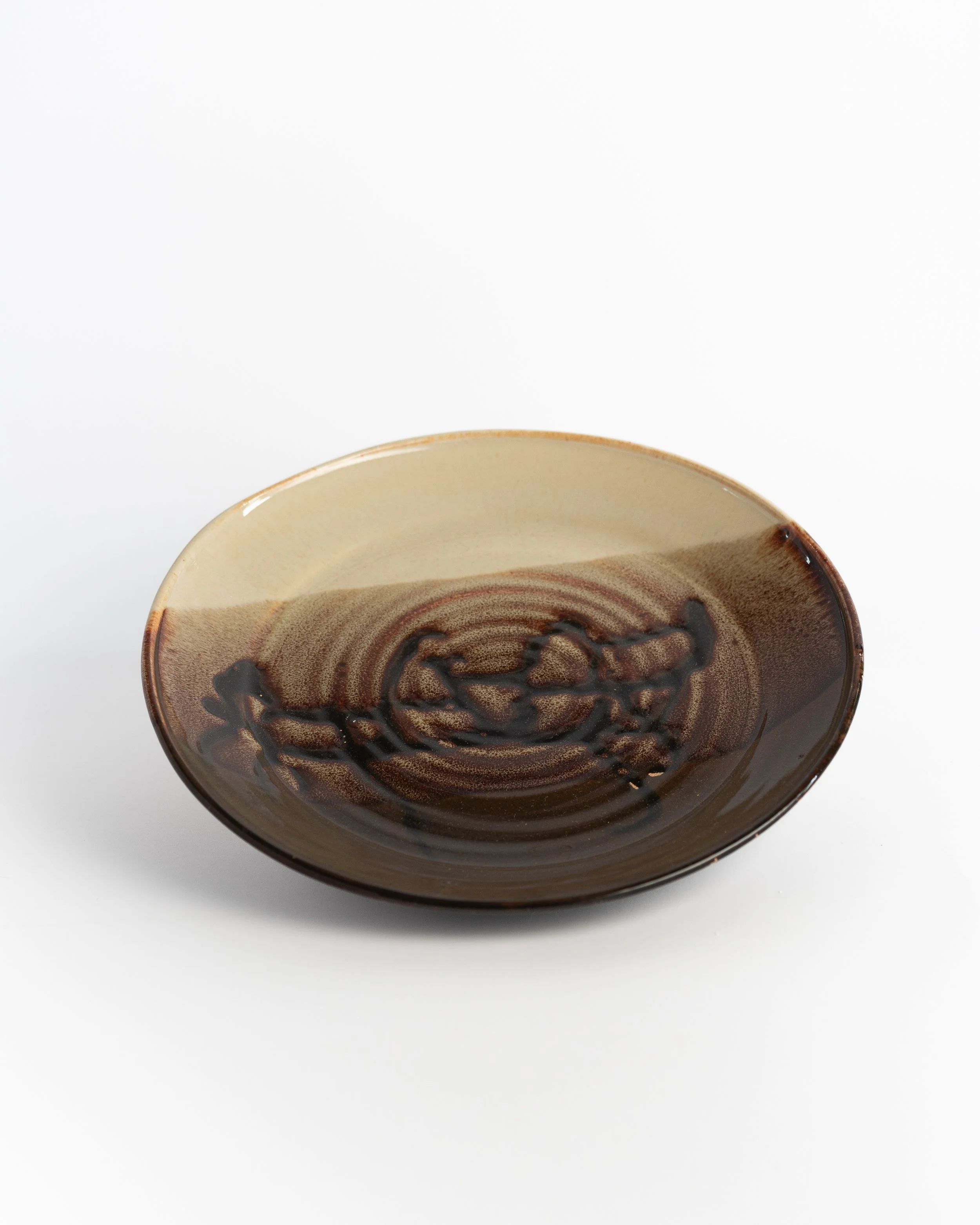 Shallow ceramic plate in cream and glossy brown with a swirling tortoiseshell pattern at its center.