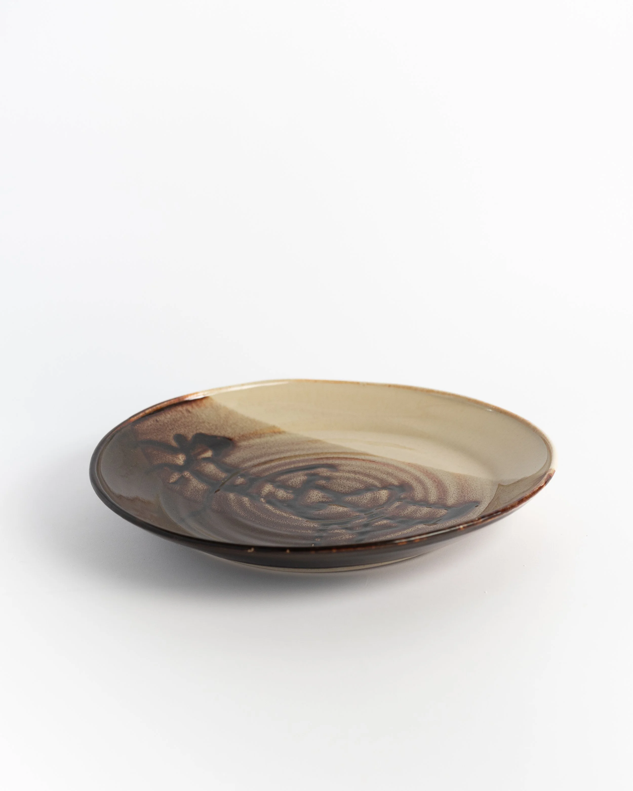 Cream and brown ceramic plate seen edge-on, dark glaze breaking across the rim.