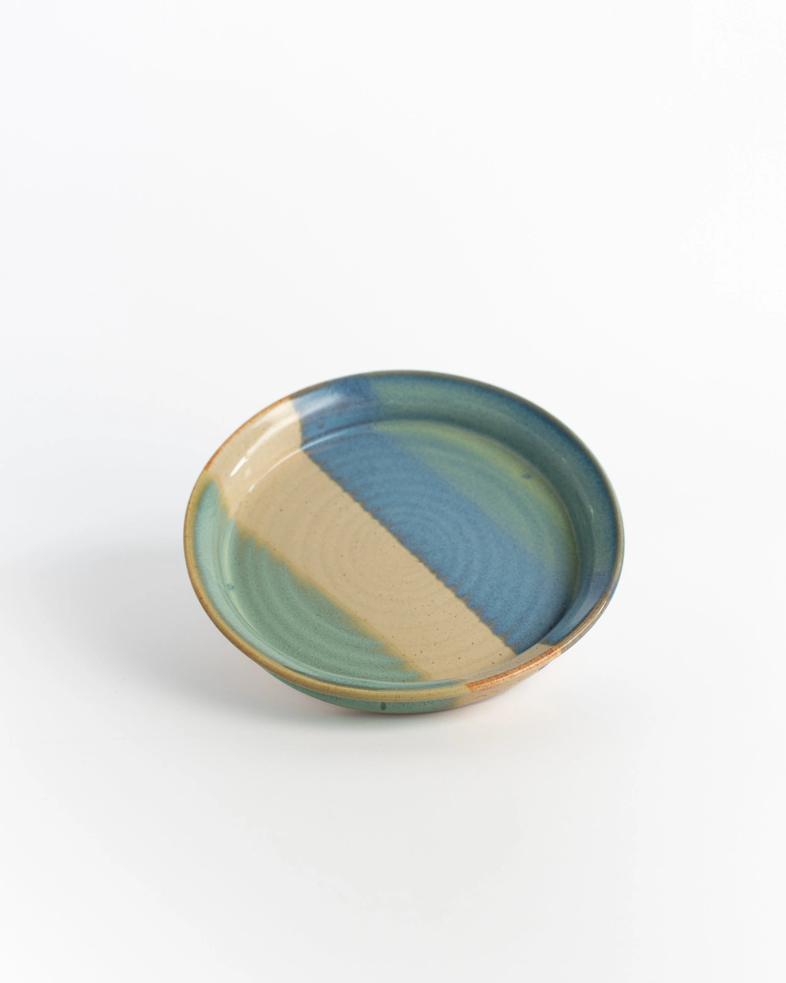 Shallow rimmed ceramic plate in blue and sea green with a wide band of bare sand across the center.