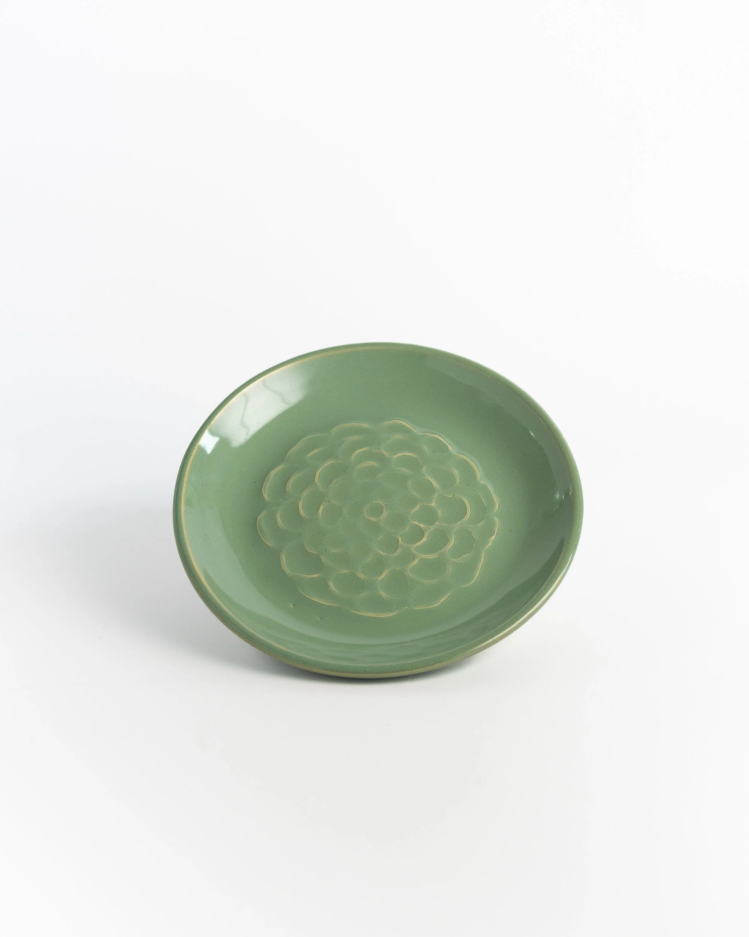 Small round ceramic plate in soft celadon green with a stamped chrysanthemum at its center.
