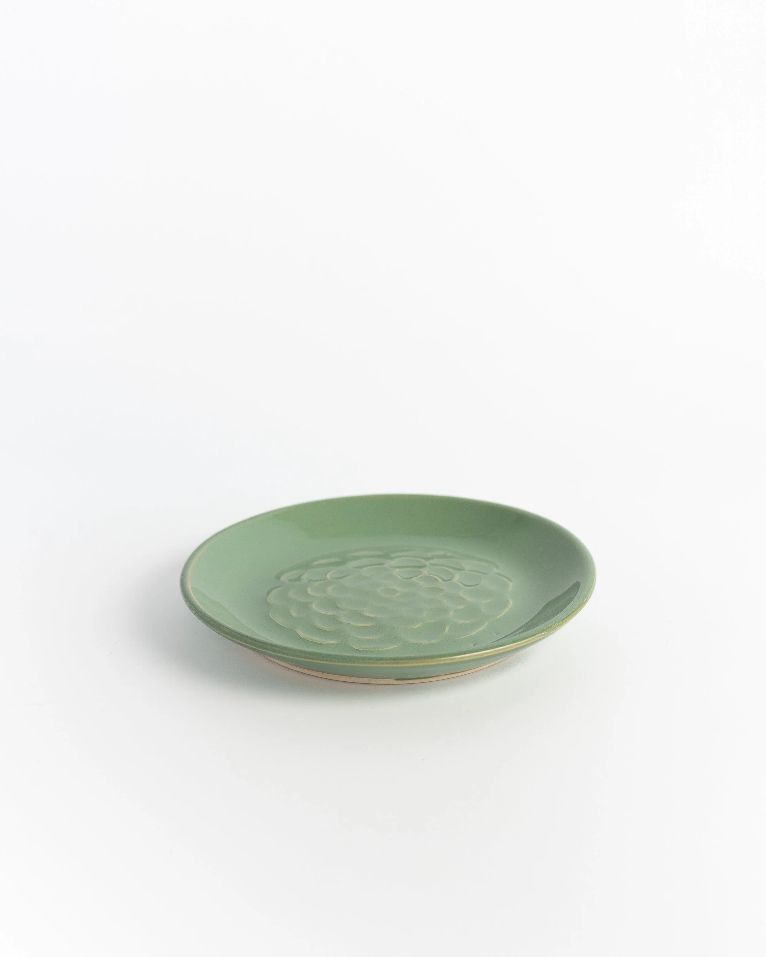 Celadon green ceramic plate seen edge-on, the stamped flower catching the light.