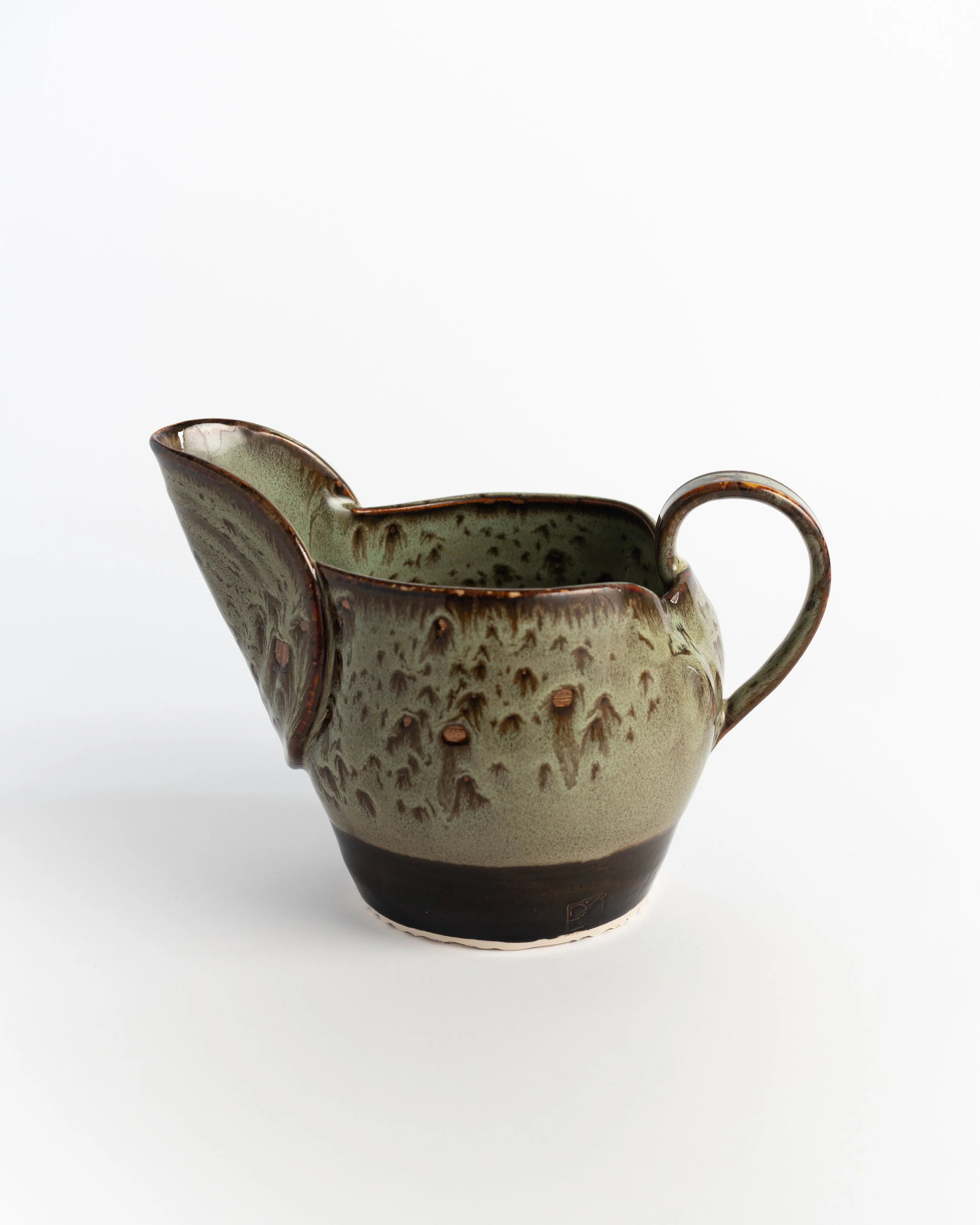 Small ceramic pitcher in speckled moss green over a dark chocolate base, with a wide pouring lip.