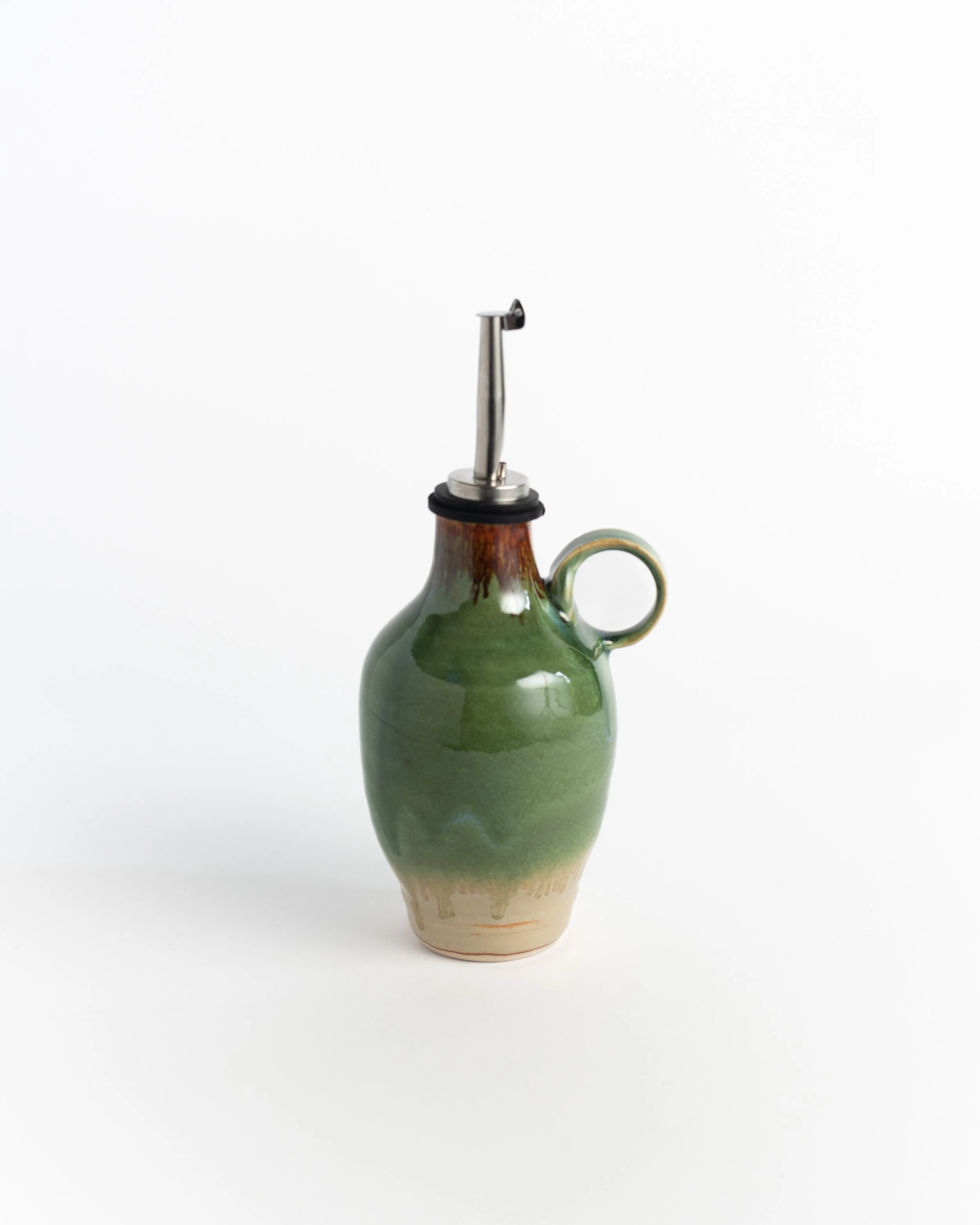 Handled ceramic oil jug in glossy emerald green fading to bare clay, with a stainless pour spout.
