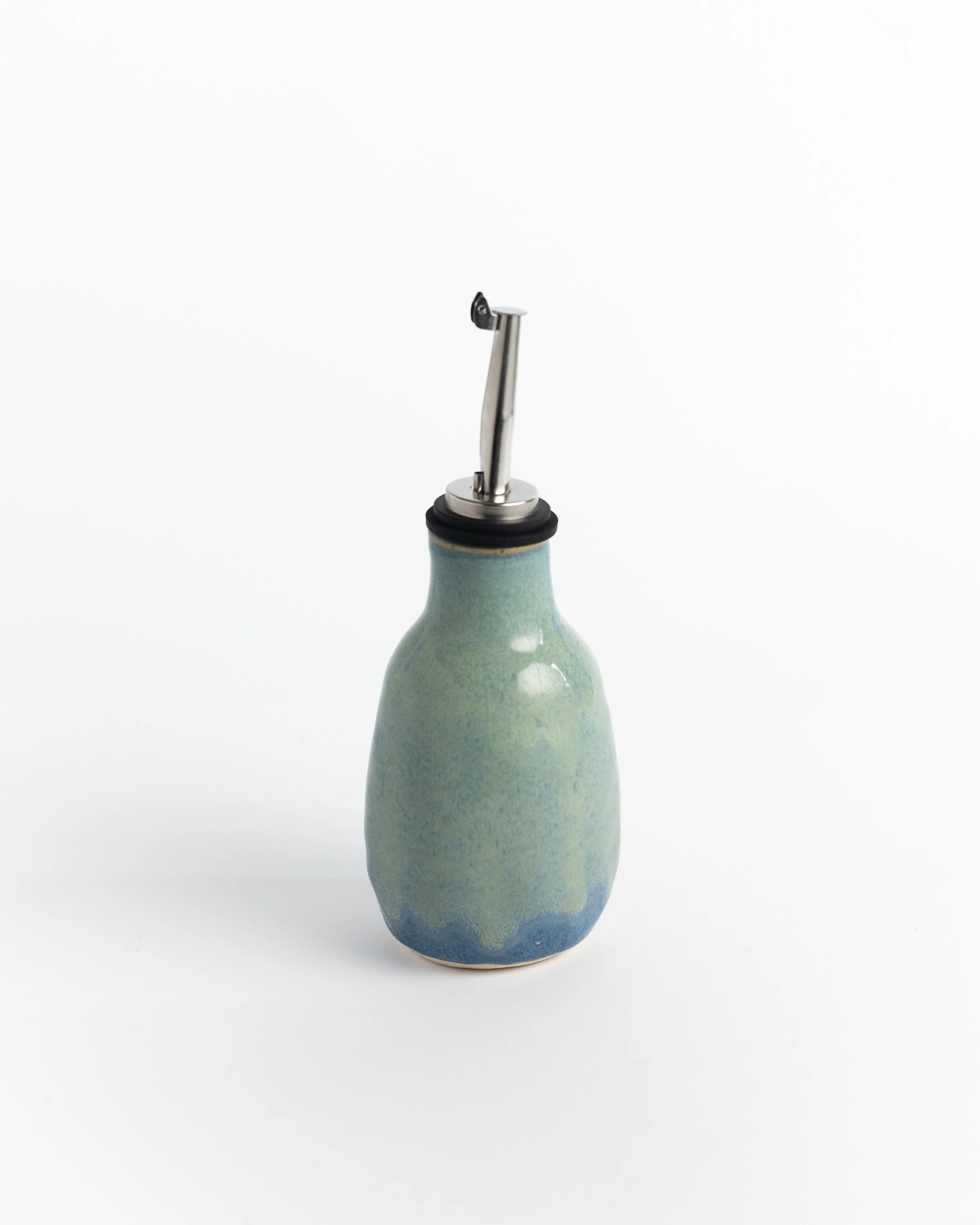 Ceramic oil cruet in seafoam green with cobalt pooling at the base and a stainless pour spout.