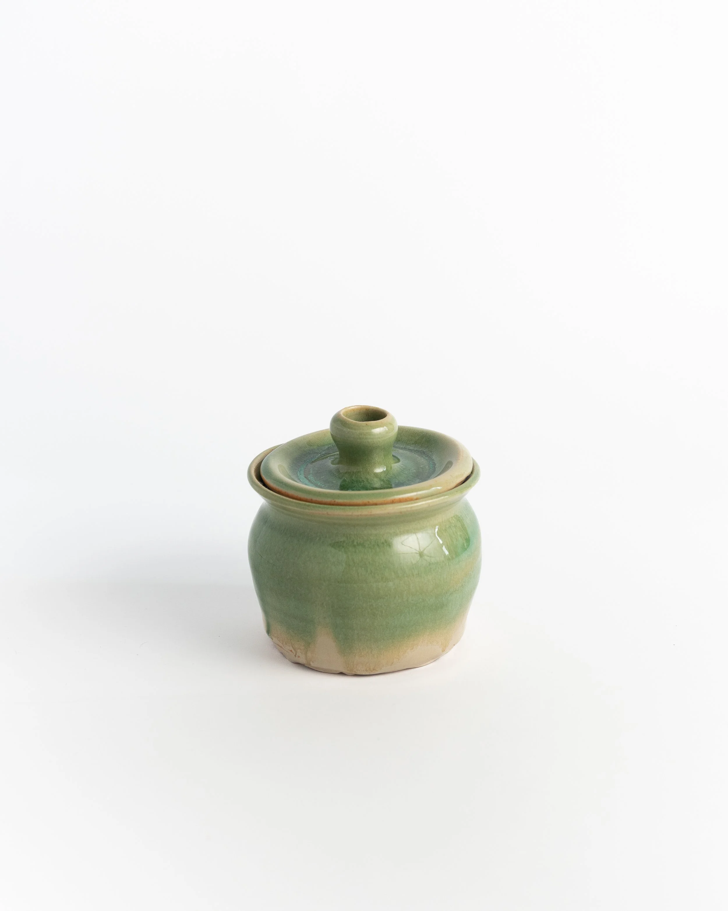 Small lidded ceramic jar in soft green over bare clay, with a knobbed lid.
